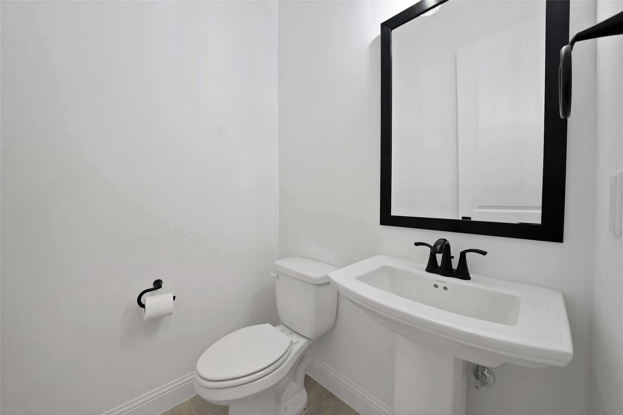 Pedestal sink featuring a matte black widespread faucet, rectangular mirror with a black frame, and matching matte black hardware