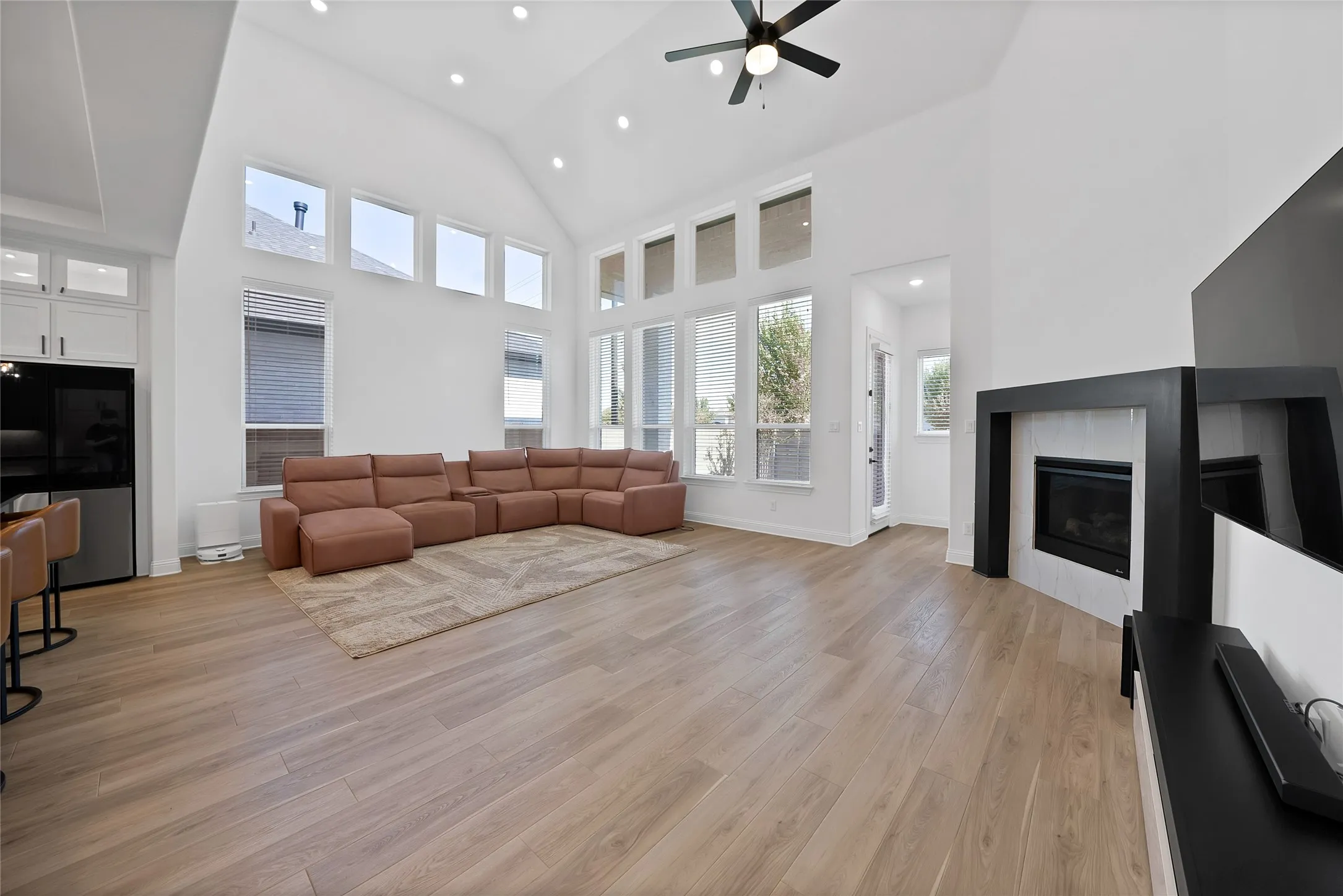 Vaulted ceilings, expansive windows, wood-finish flooring, recessed lighting, and a fireplace with a black mantle