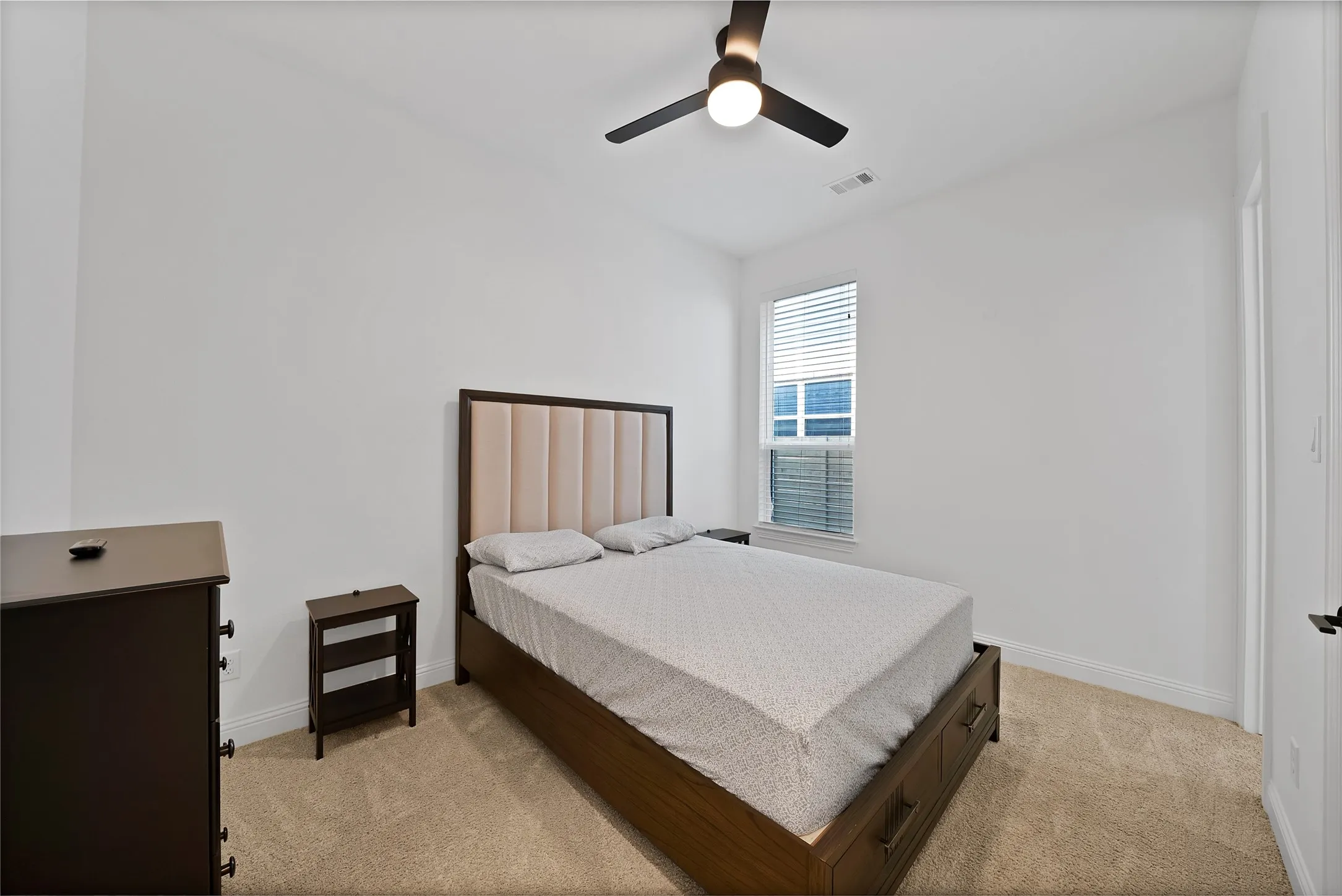 Room featuring neutral wall-to-wall carpeting, a singular window with integrated blinds, and a ceiling-mounted light fixture with a fan