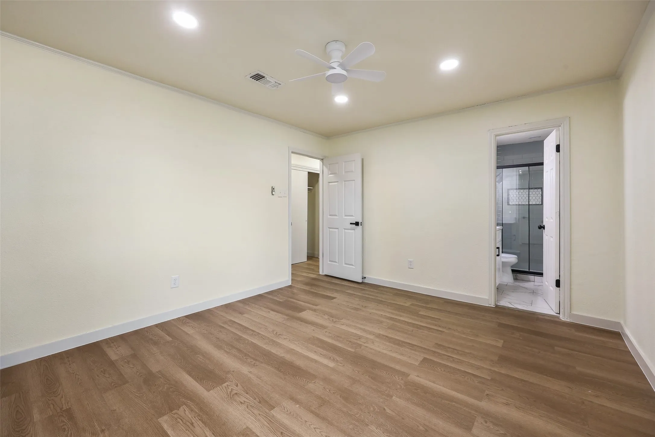 Wood-finish flooring, recessed lighting, and a ceiling fan illuminate this space