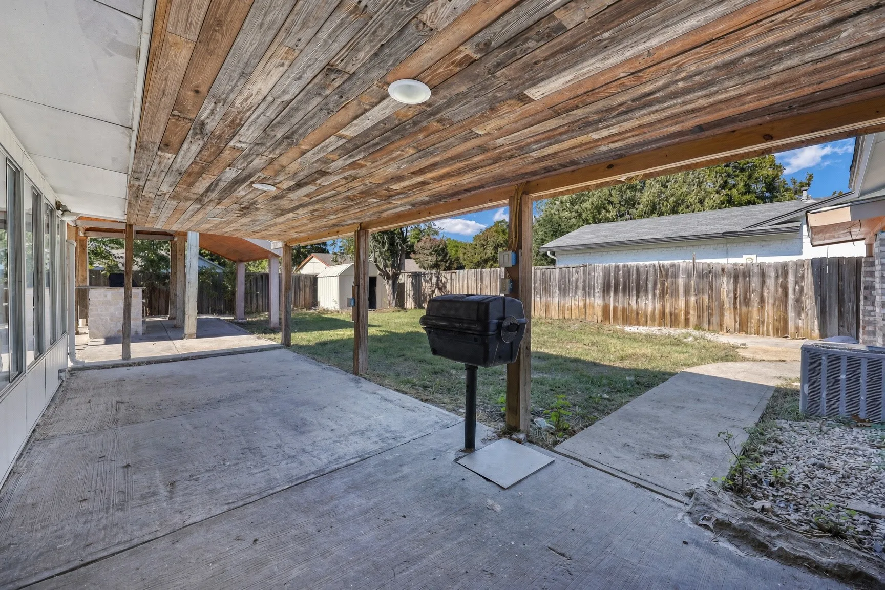 Covered patio with a wood-plank ceiling, concrete flooring, and an expansive fenced yard