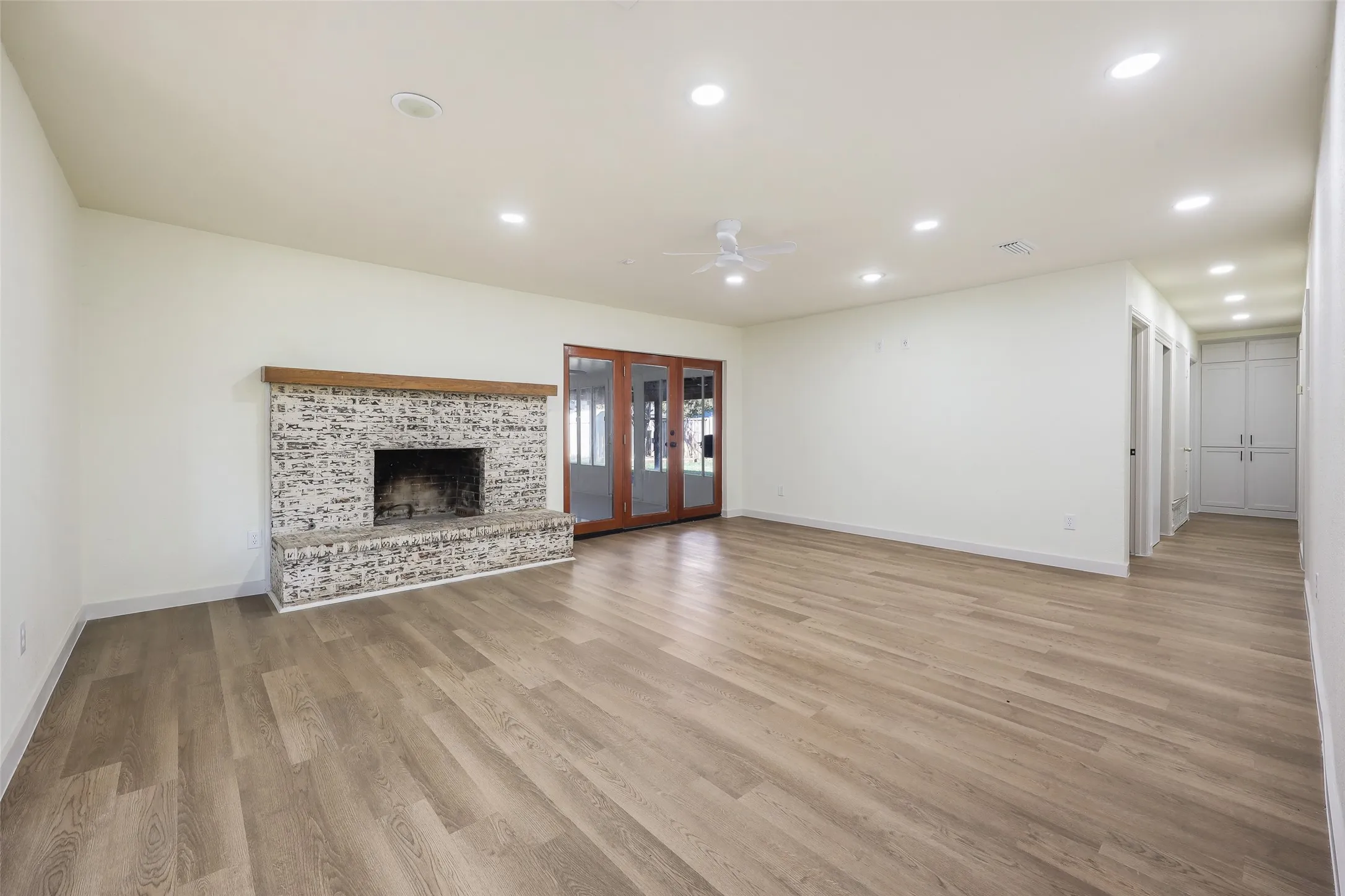 Spacious room featuring wood-finish flooring, a brick fireplace with a wood mantel, recessed lighting, and built-in cabinetry