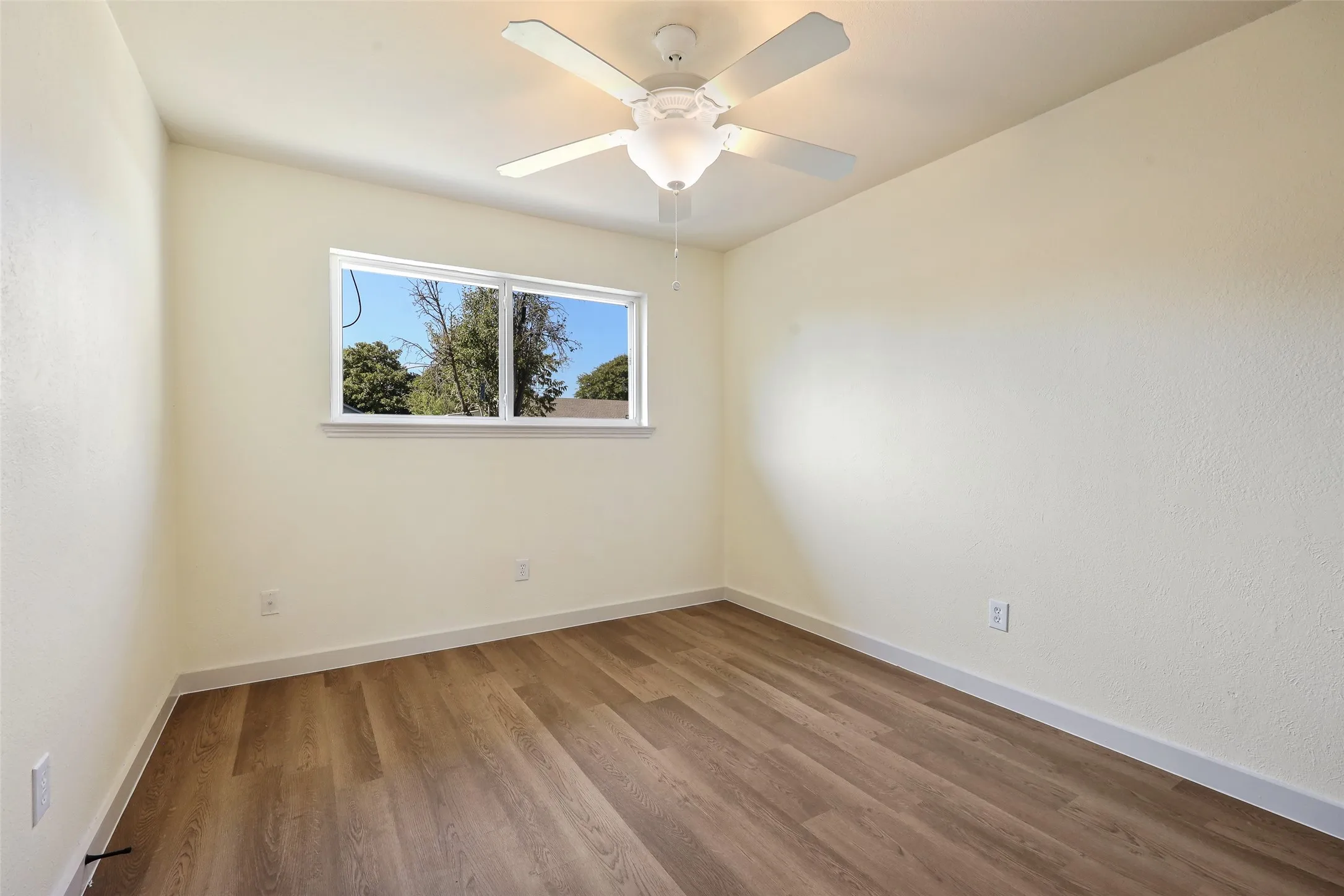 Wood-finish flooring, white walls, and a ceiling fan with integrated lighting