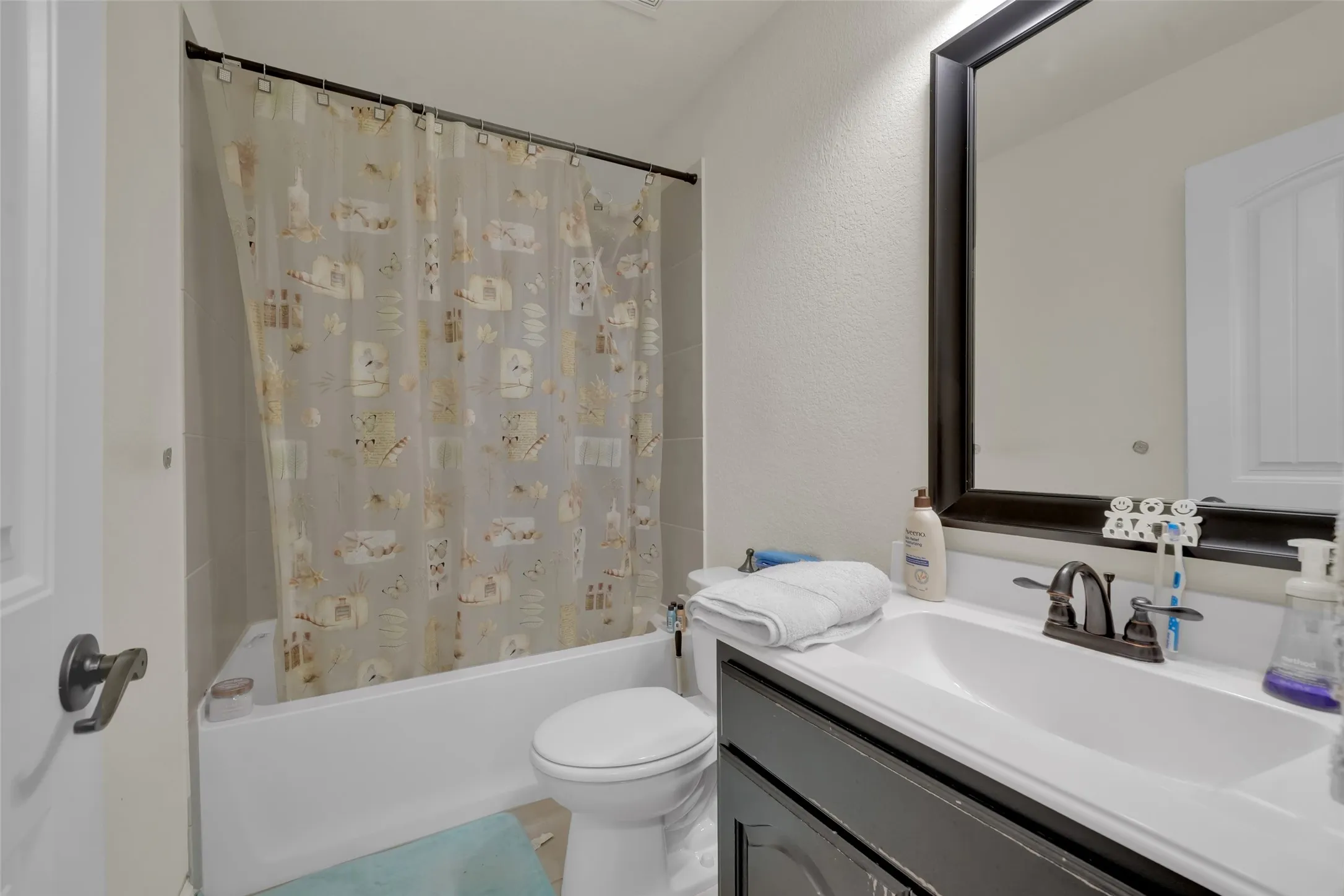 Bathroom featuring a dark wood-finish vanity with an integrated white sink, dual-handle oil-rubbed bronze faucet, dark-framed mirror, and a tub-shower combination with tile surround