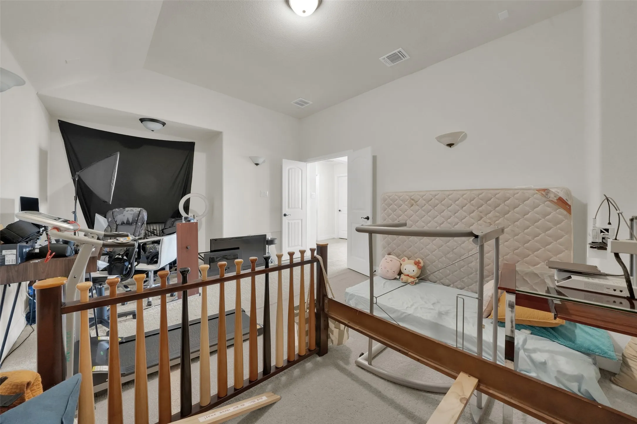 High-ceiling interior featuring a stepped tray ceiling, dual wall-mounted light fixtures, carpeted flooring, and a wooden balustrade