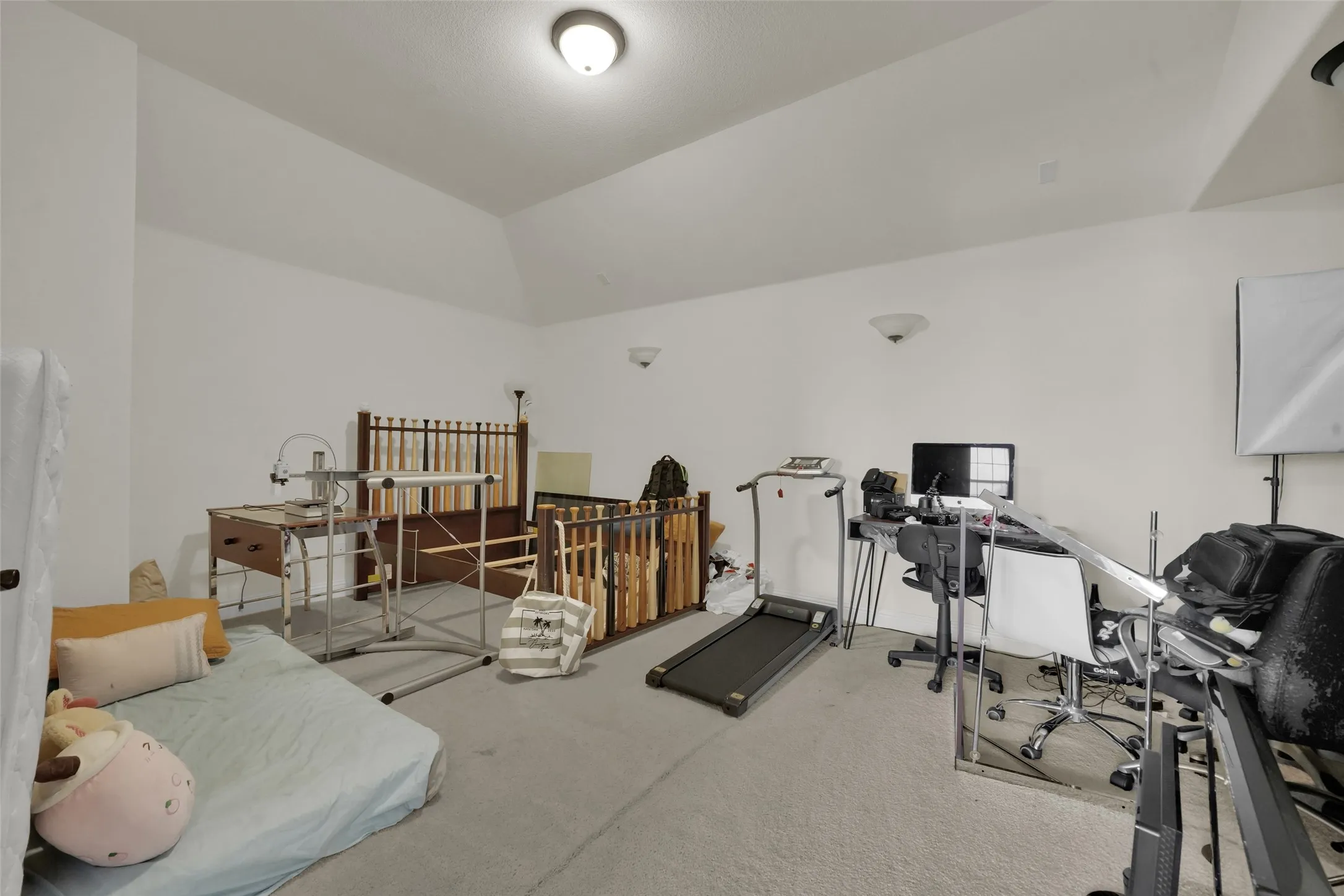 Vaulted ceiling, neutral wall finish, wall-mounted sconce lighting, and wood baluster stair railing