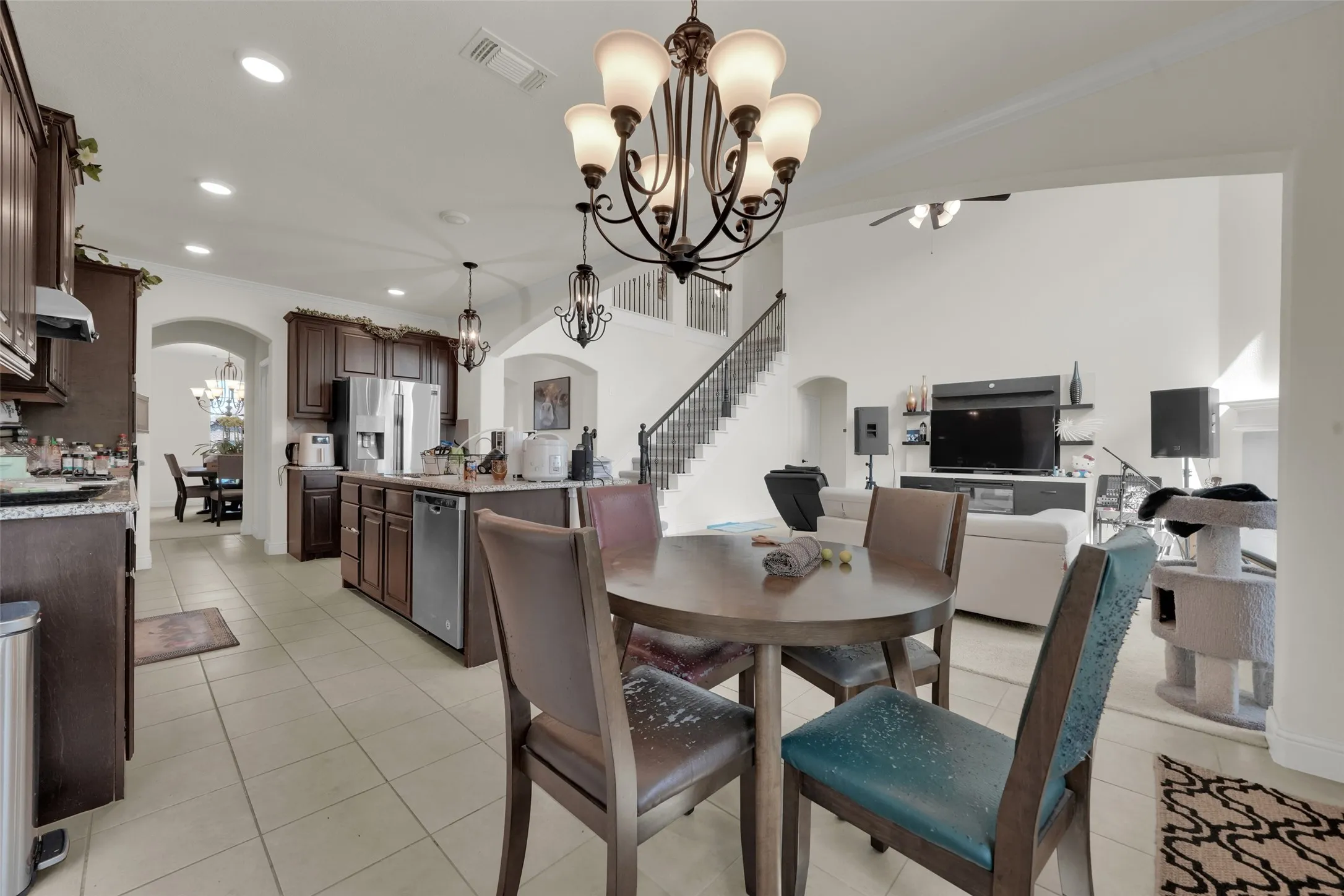 Open-concept interior featuring high ceilings, dark stained wood cabinetry, stone countertops, tiled flooring, and a multi-tiered chandelier