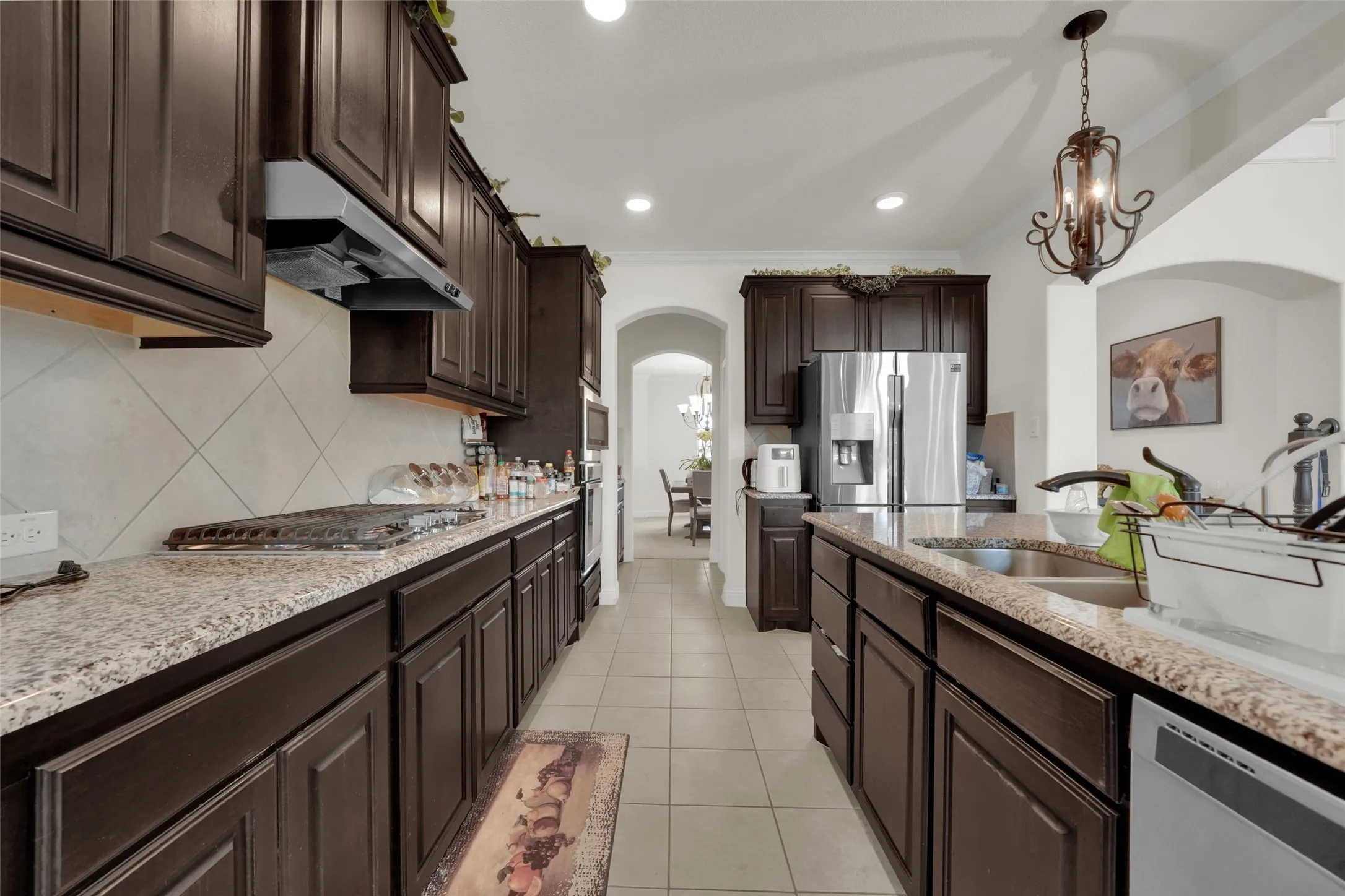 Kitchen featuring stained wood cabinetry, stone-surface countertops, tile backsplash, stainless steel appliances, and a hanging pendant light fixture
