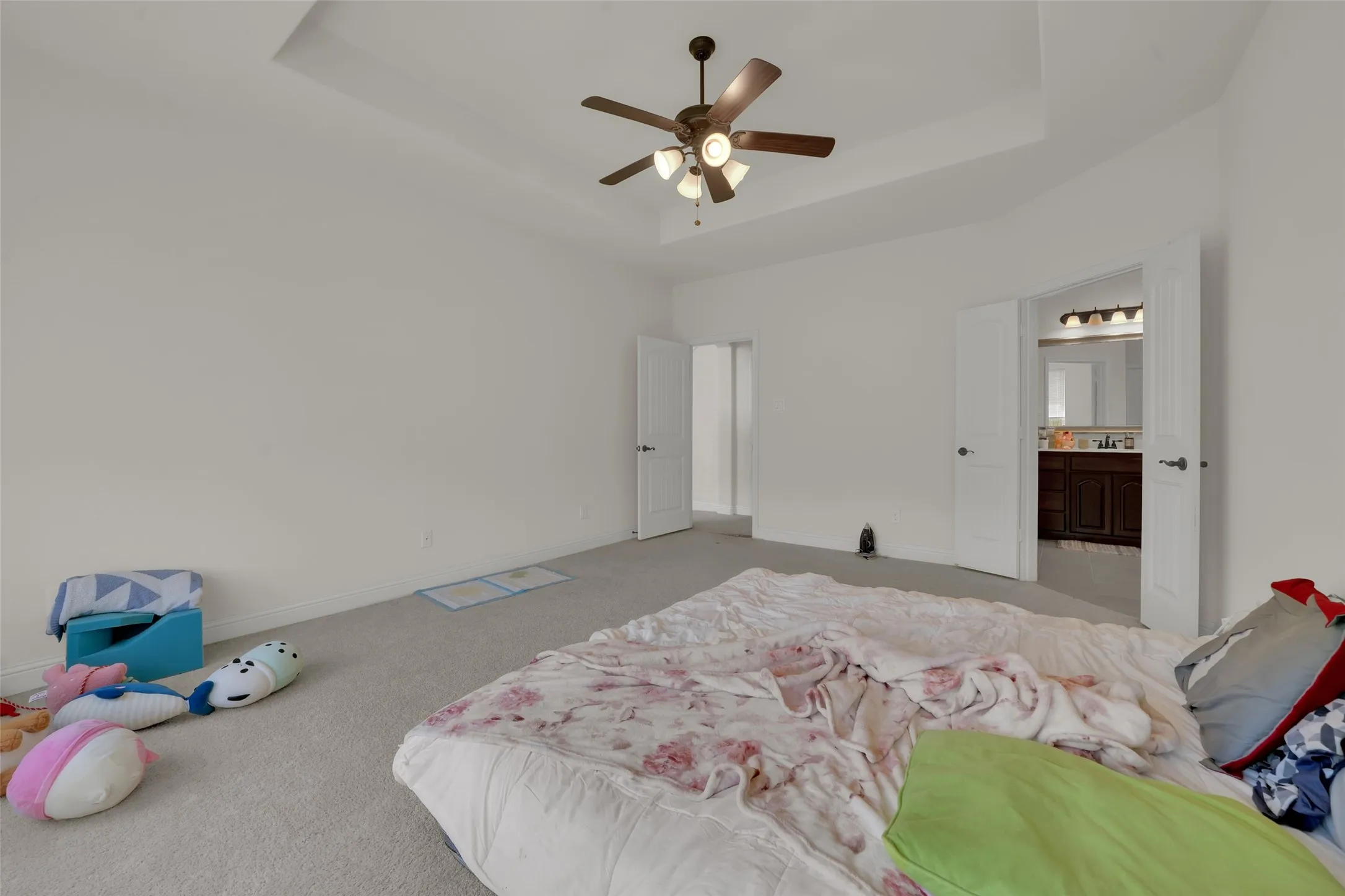 Tray ceiling featuring a central multi-blade ceiling fan with integrated lighting, wall-to-wall carpeting, and double-door entry