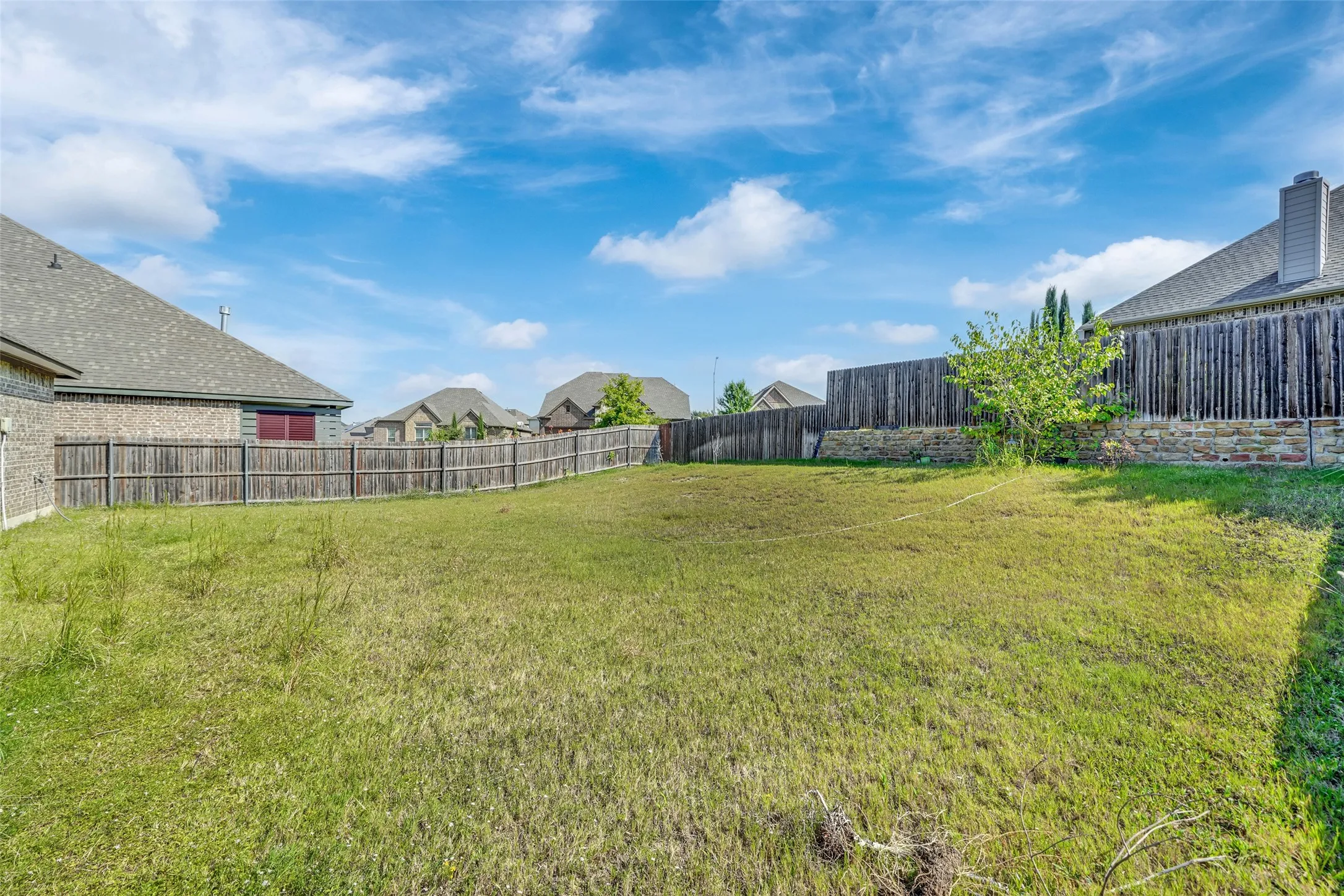 Backyard featuring a grass lawn, perimeter wood fencing, and a stone retaining wall