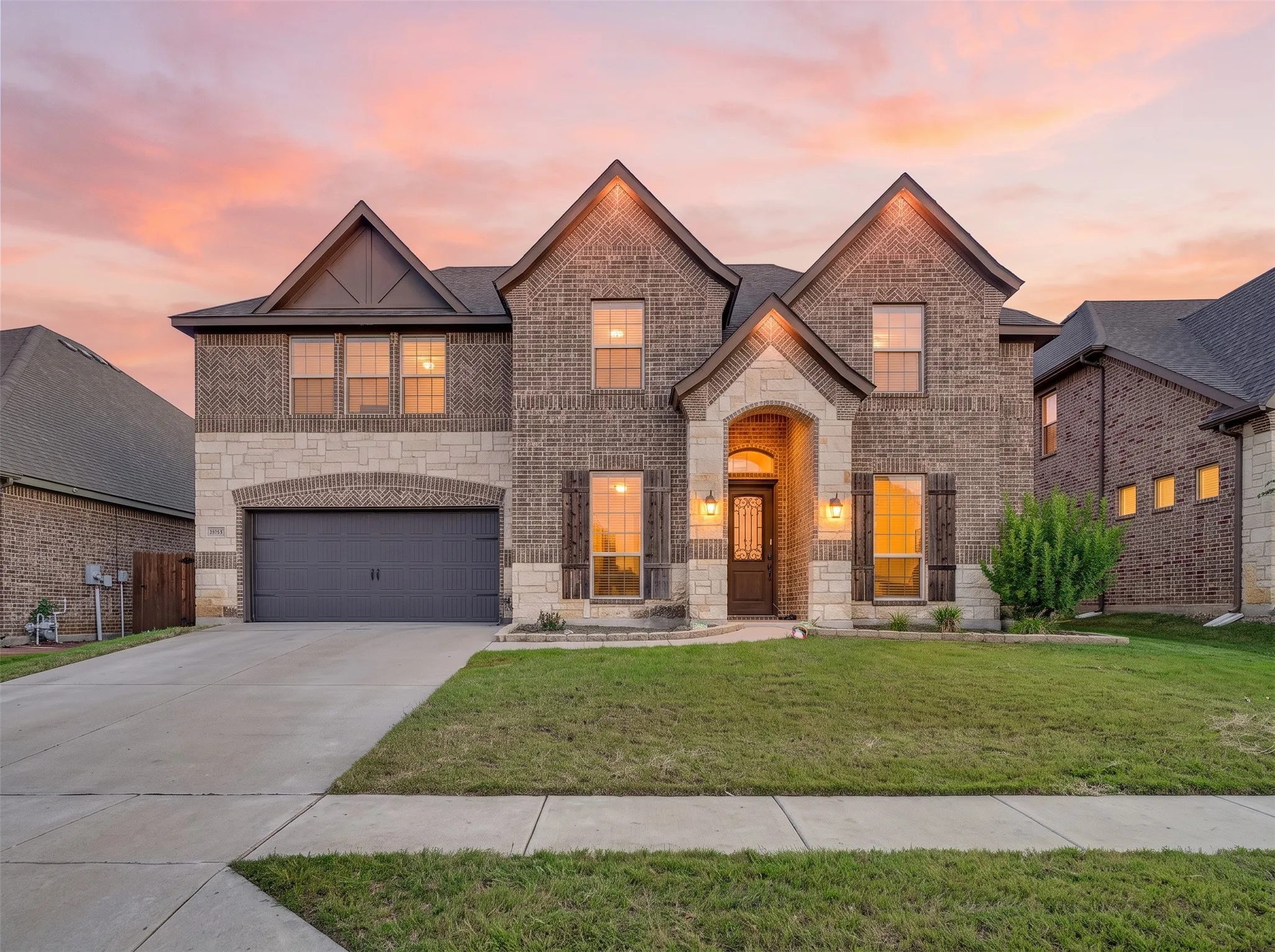 Two-story brick and stone facade featuring a covered entryway, decorative shutters, multi-gabled roofline, and a multi-car garage