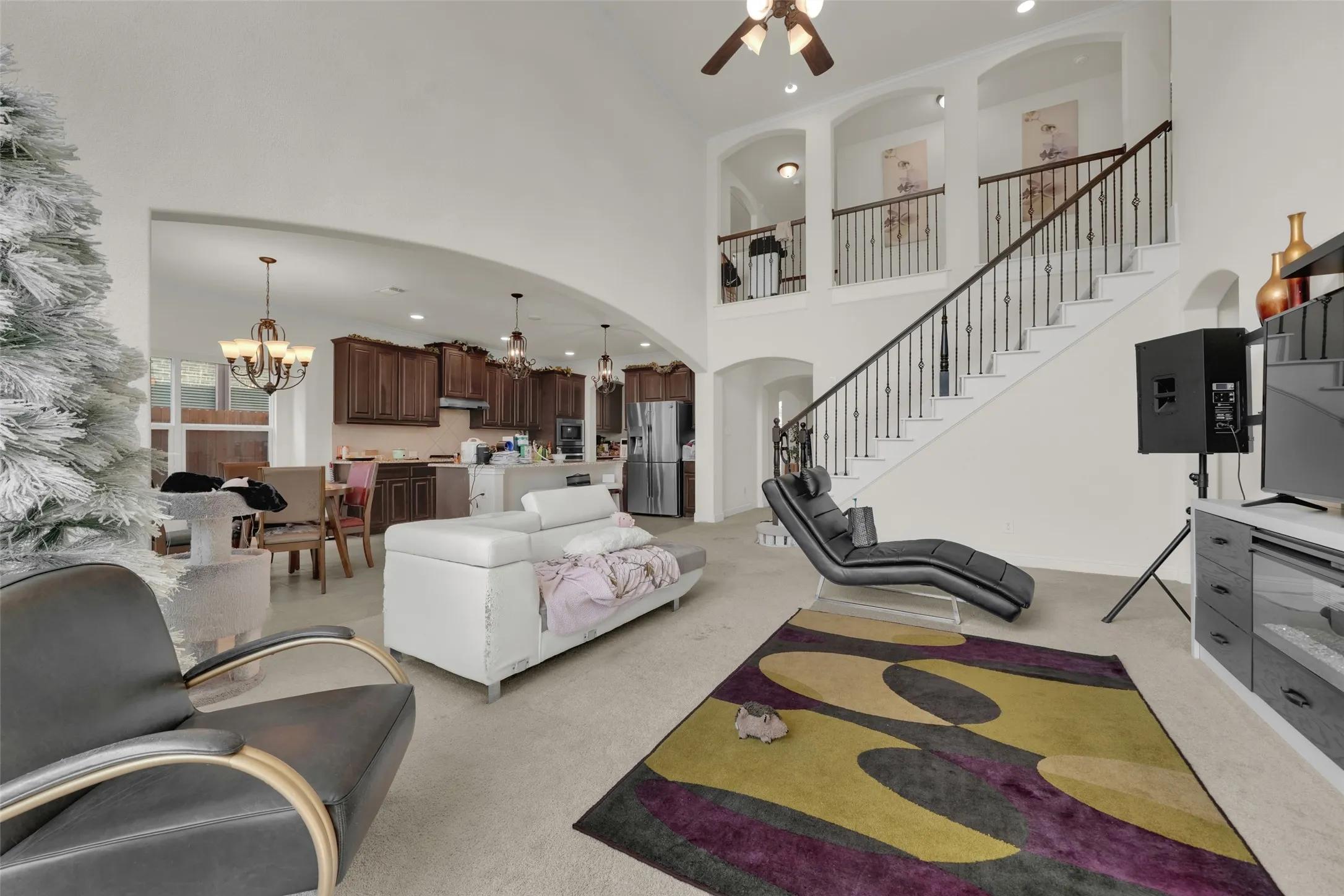Open-concept interior featuring vaulted ceilings, a staircase with decorative metal balusters, arched architectural detailing, recessed lighting, and custom wood cabinetry