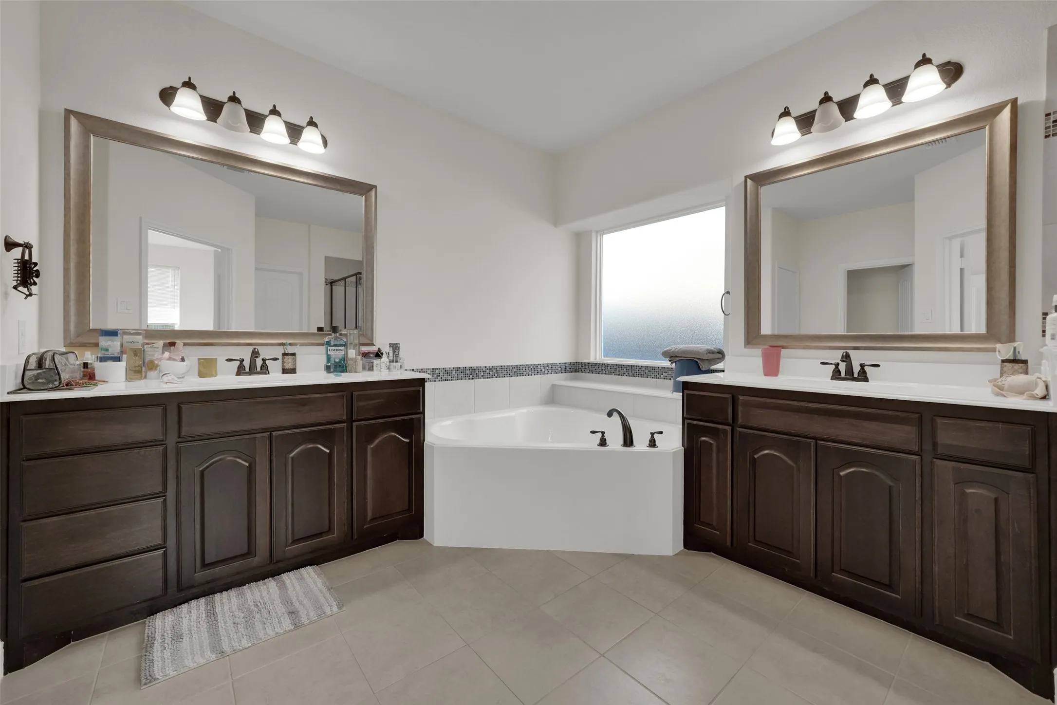 Dual vanities with dark-finish cabinetry, solid-surface countertops, framed mirrors, and a corner soaking tub
