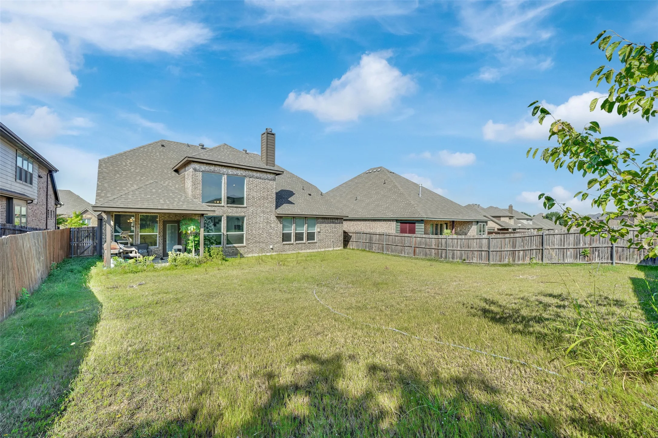 Brick exterior, covered patio, multi-pane windows, chimney, and wooden perimeter fencing