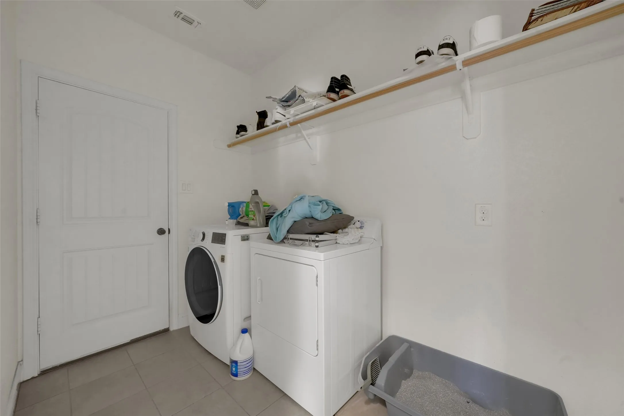 Utility room featuring large-format tile flooring, a solid-core paneled door, and an expansive wall-mounted shelf
