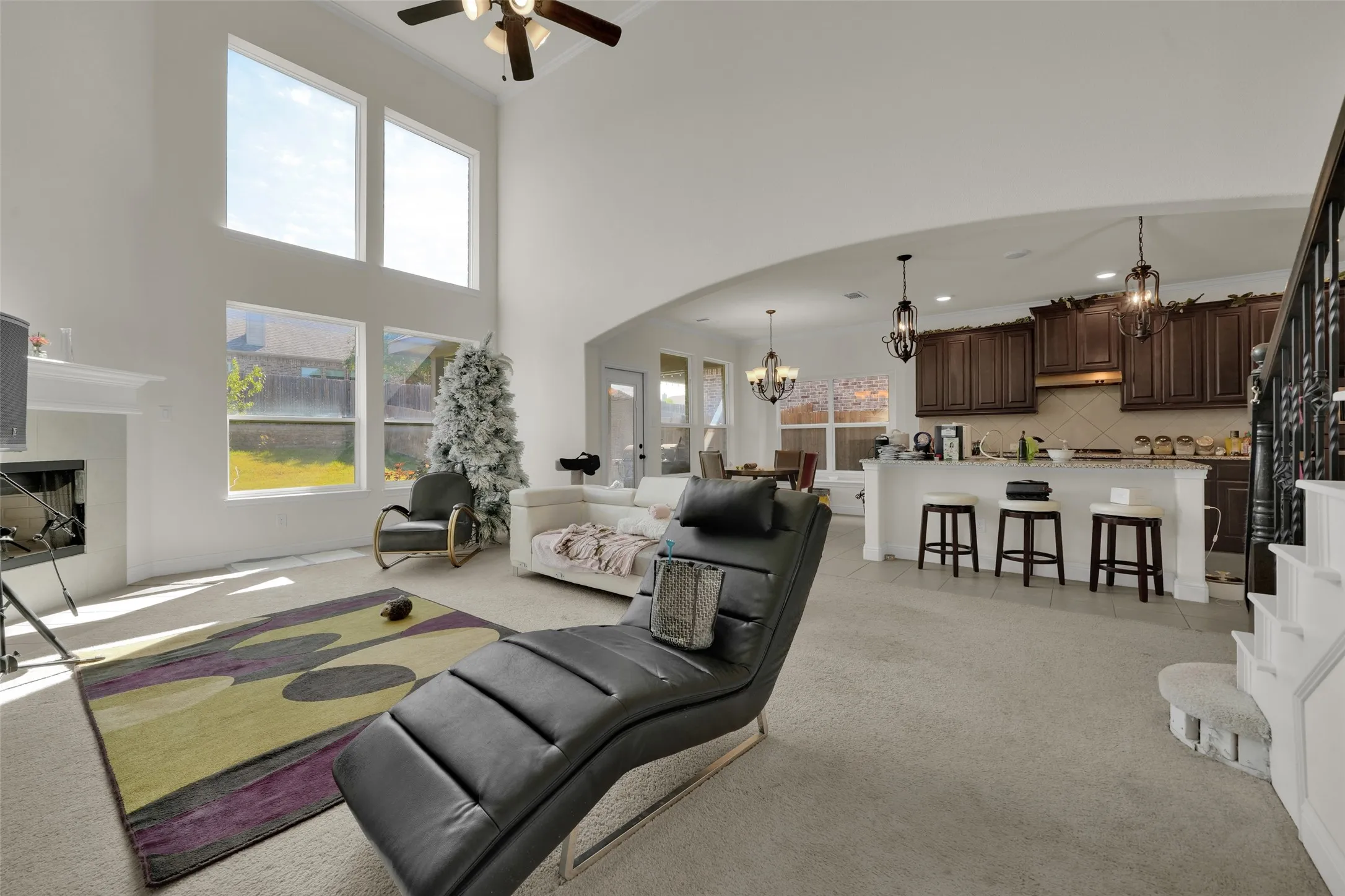 Open-concept interior featuring a vaulted ceiling, floor-to-ceiling windows, a fireplace with a mantel, an eat-in kitchen island, and custom dark wood cabinetry