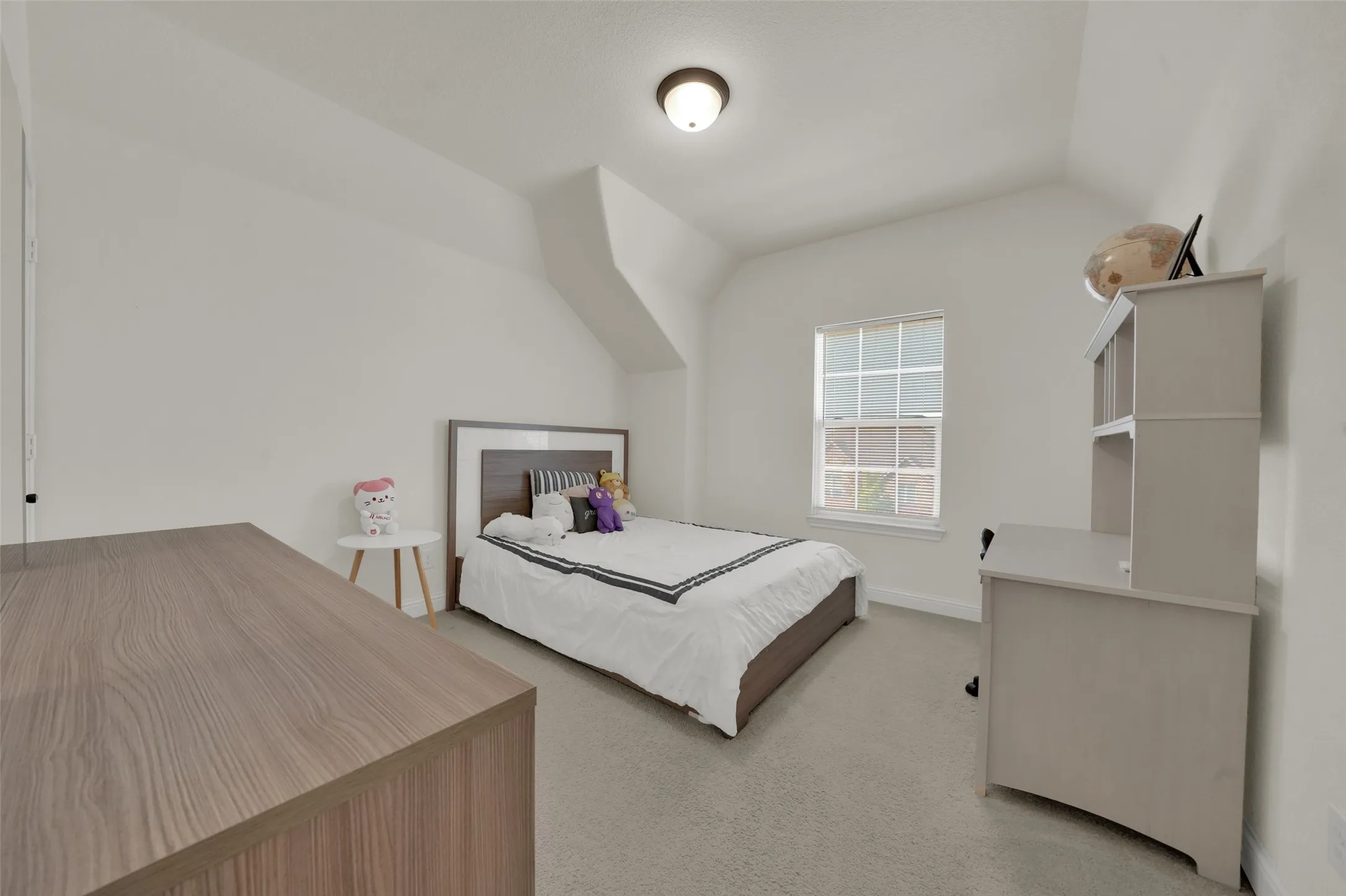 Neutral-toned interior space featuring vaulted ceilings, wall-to-wall carpeting, and a multi-pane window