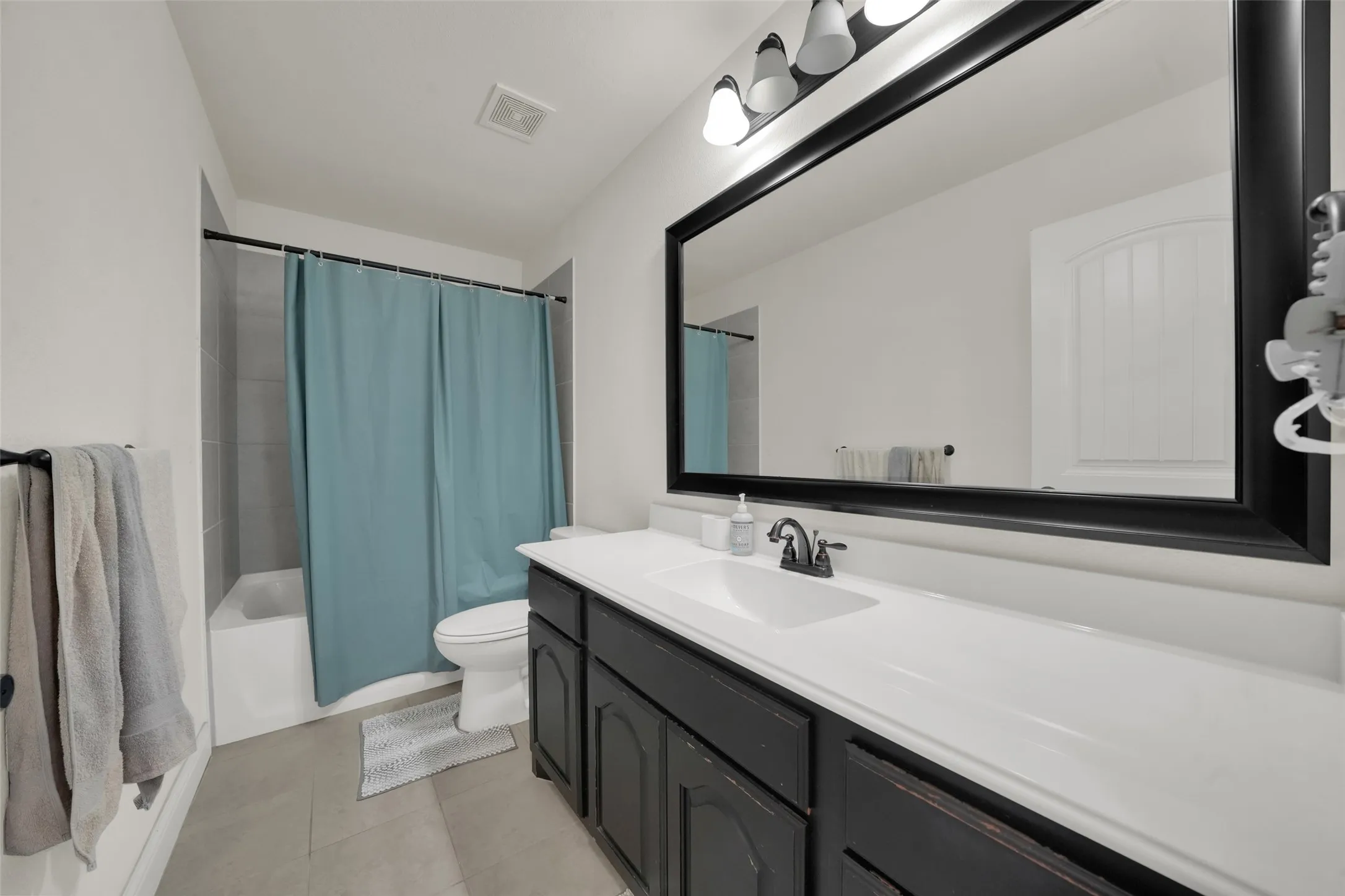 Bathroom featuring a dark wood vanity with white countertop, integrated sink, large wall-mounted mirror with a black frame, and a three-light fixture