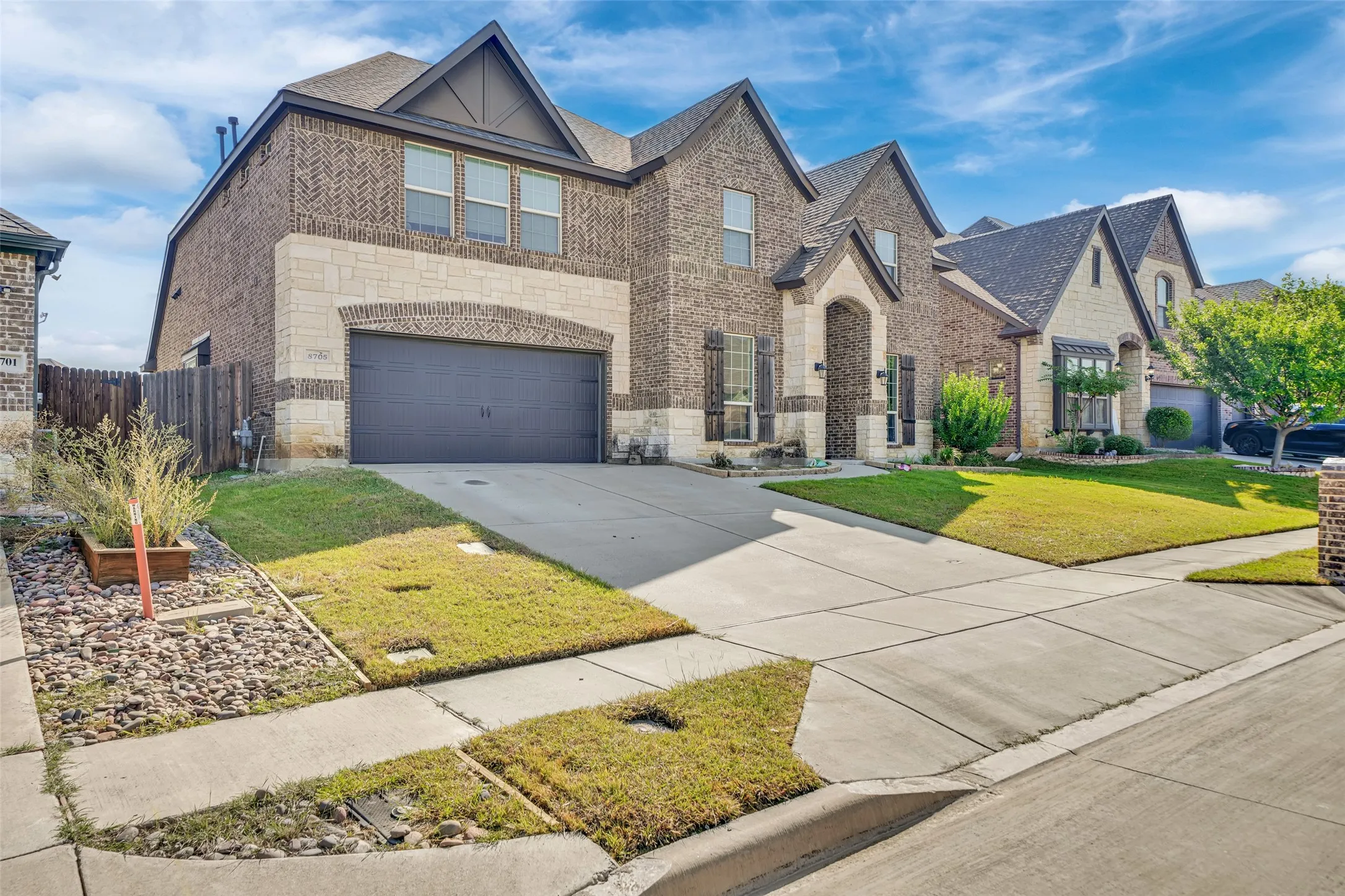 Two-story exterior featuring a brick and masonry facade, multiple gables, an attached garage, and a concrete driveway