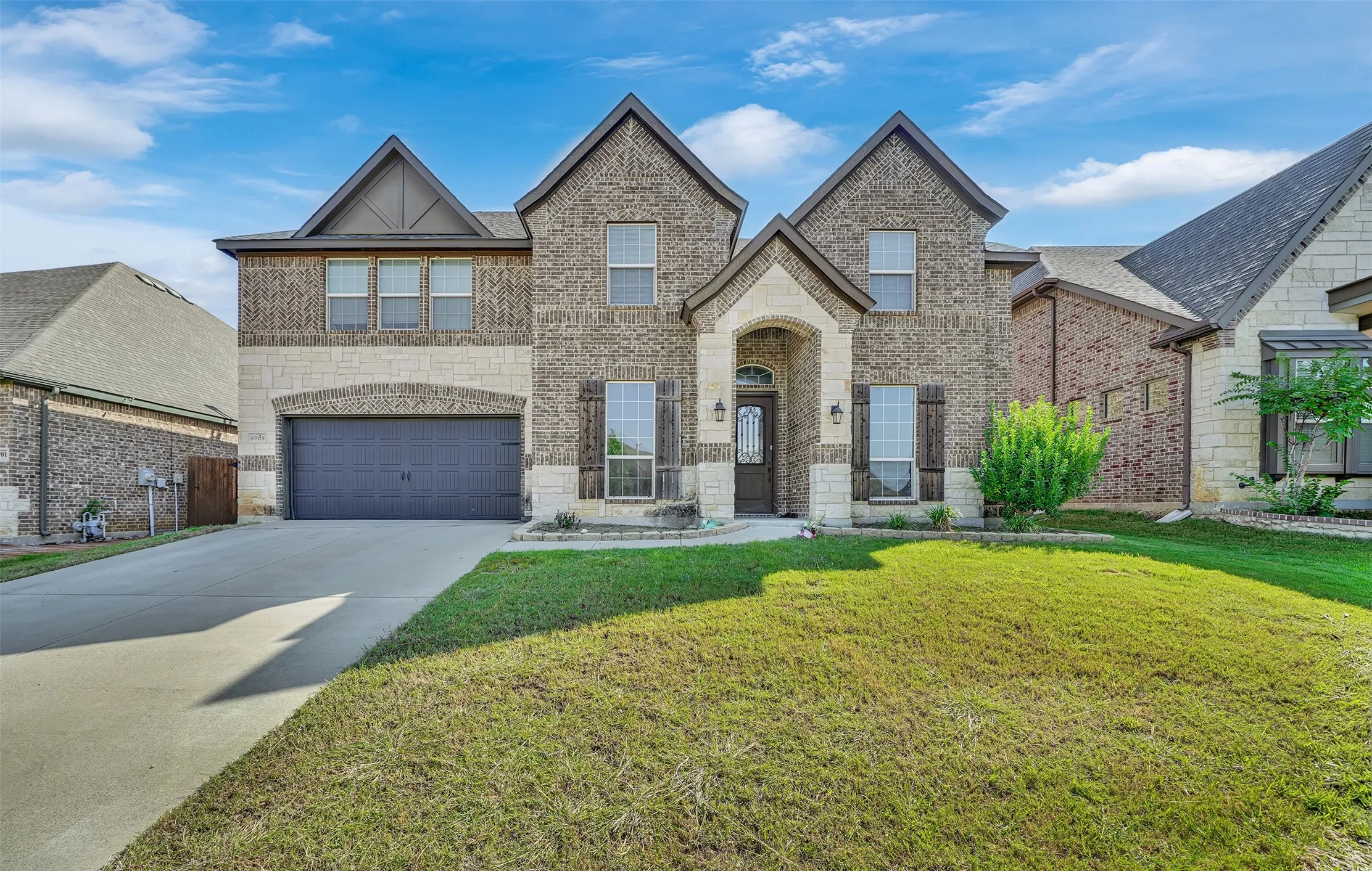 Two-story brick and stone facade featuring a multi-gabled roofline, recessed entryway, decorative shutters, and an attached two-car garage