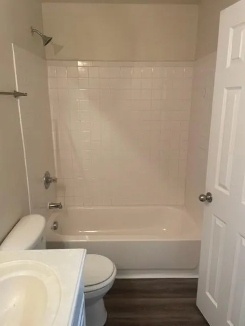 Full bathroom featuring a tub-shower combination with white wall tile, a pedestal sink, and wood-finish flooring