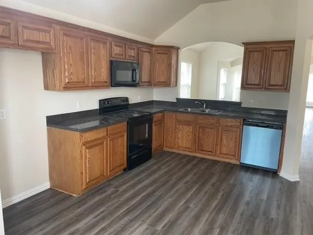 Kitchen featuring stained wood cabinetry, dark countertops, wood-finish flooring, and a vaulted ceiling with arched pass-through
