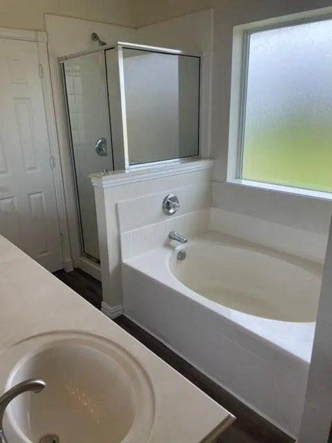 Bathroom featuring a built-in soaking tub, separate stall shower with glass enclosure, single-basin vanity with solid-surface countertop, and privacy window