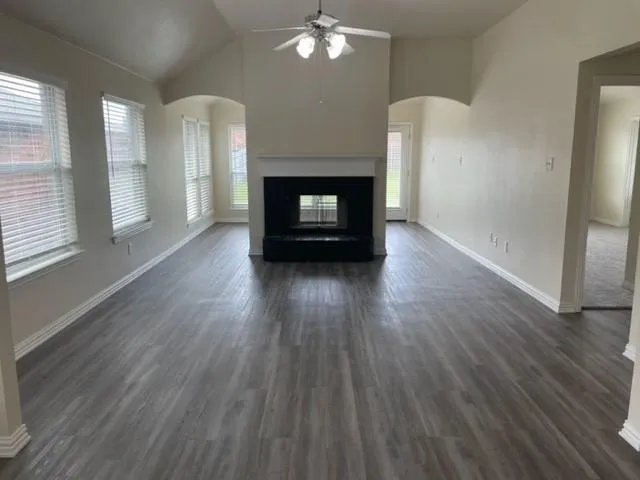 Vaulted ceilings, wood-finish flooring, central fireplace with a decorative mantle, arched architectural openings, and multiple windows providing natural light