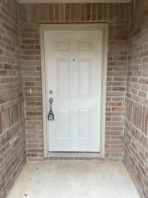 Entryway featuring a solid white six-panel door framed by tan brick masonry and concrete flooring