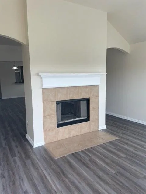 Fireplace featuring a tile surround, hearth, and painted wood mantel, complemented by wood-finish flooring and arched architectural detailing