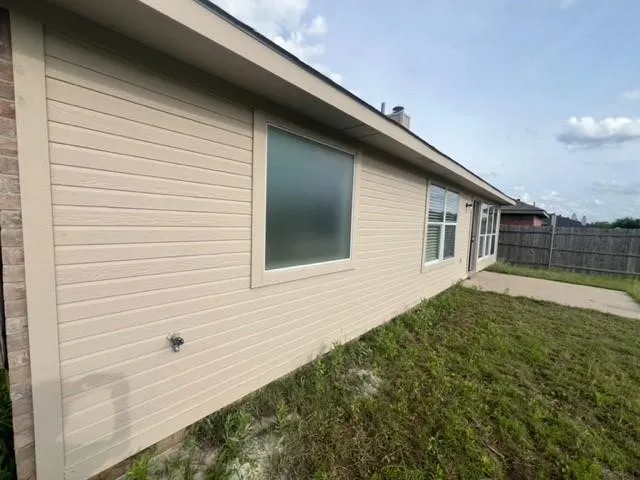 Exterior wall featuring horizontal siding, brick masonry detailing, inset windows, and a concrete patio slab