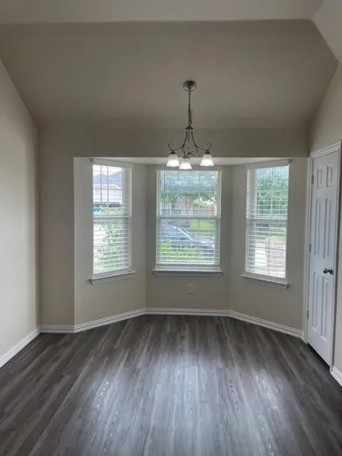 Bay window featuring three large windows, wood-finish flooring, vaulted ceiling, and an overhead multi-light fixture