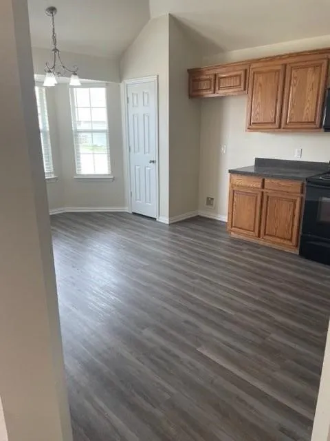Wood-finish flooring, vaulted ceiling, bay windows with natural light, wood cabinetry, and a hanging light fixture