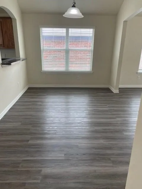 Neutral-toned interior space featuring wood-finish flooring, a pendant light fixture, and a large window with horizontal blinds