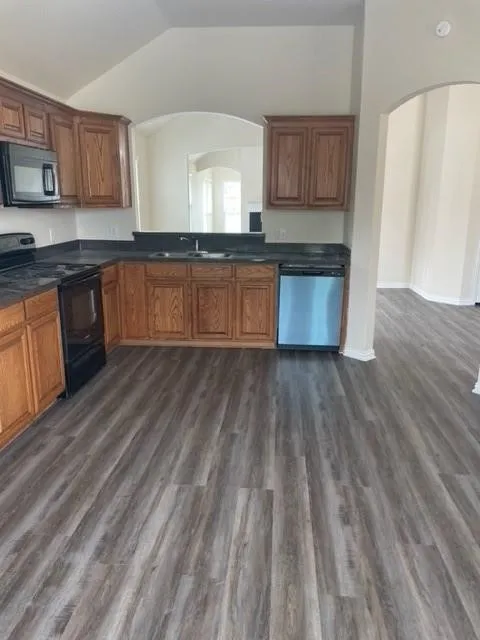 Kitchen featuring wood-finish cabinetry, dark solid-surface countertops, wood-finish flooring, and stainless steel appliances including a dishwasher and microwave