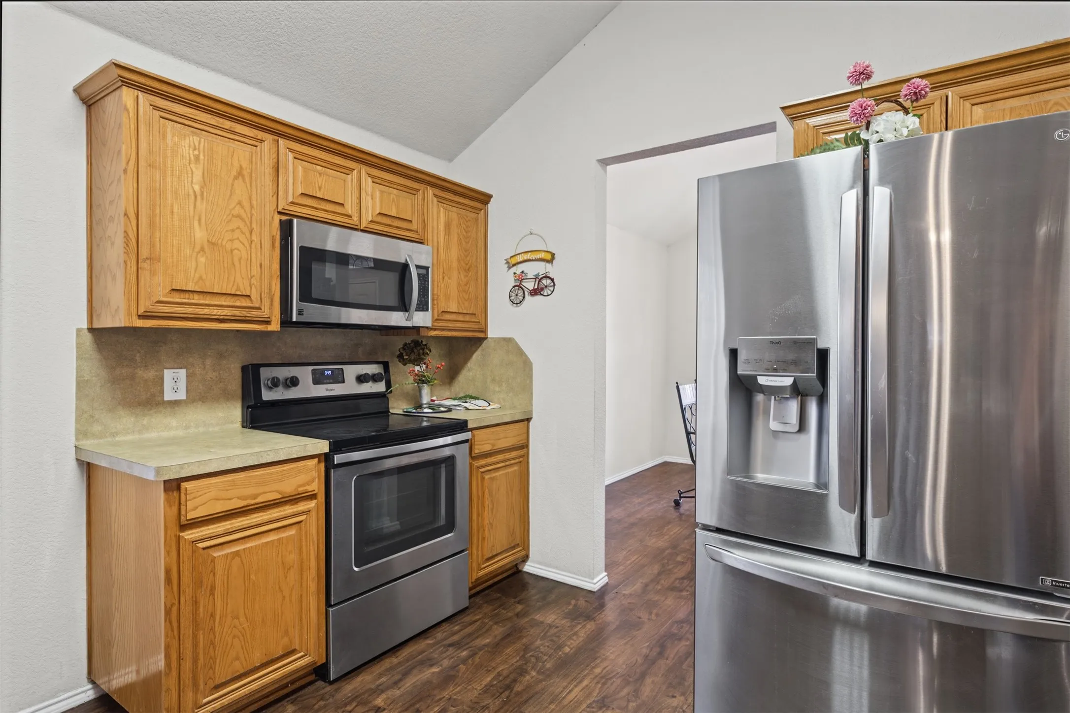 Kitchen featuring natural wood cabinetry, stainless steel appliances, a built-in microwave, stone-finish countertops, and wood-finish flooring under a vaulted ceiling