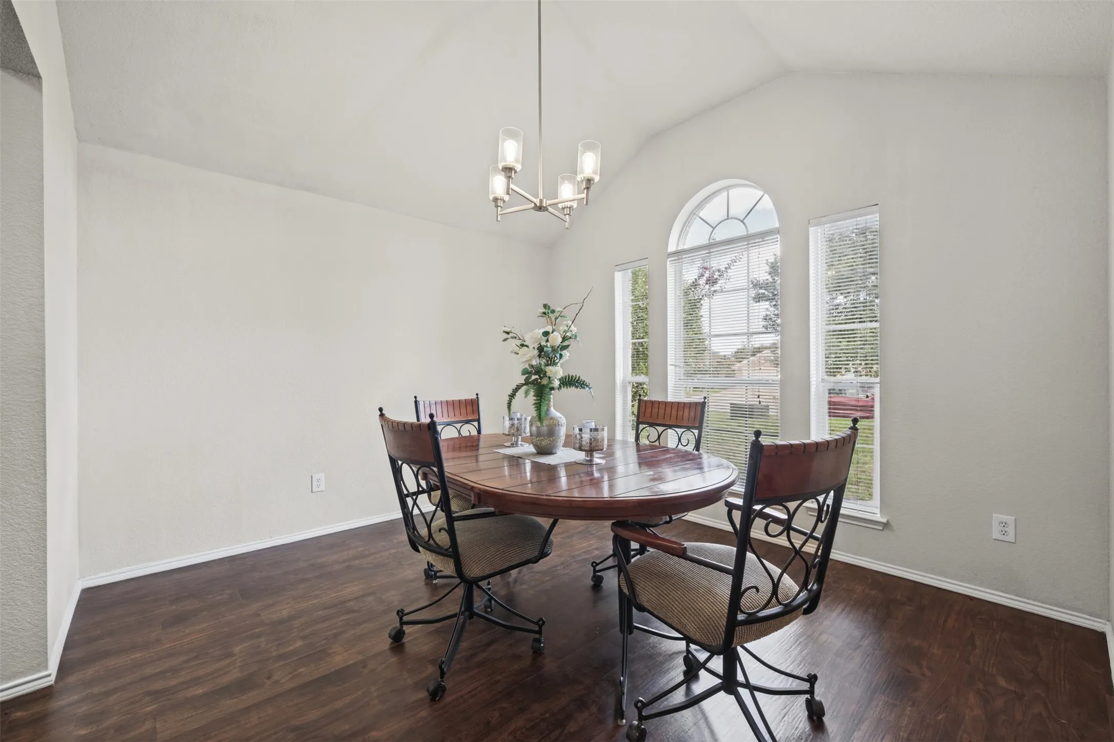 Vaulted ceiling, wood-finish flooring, multi-pane arched window, and brushed nickel finish chandelier