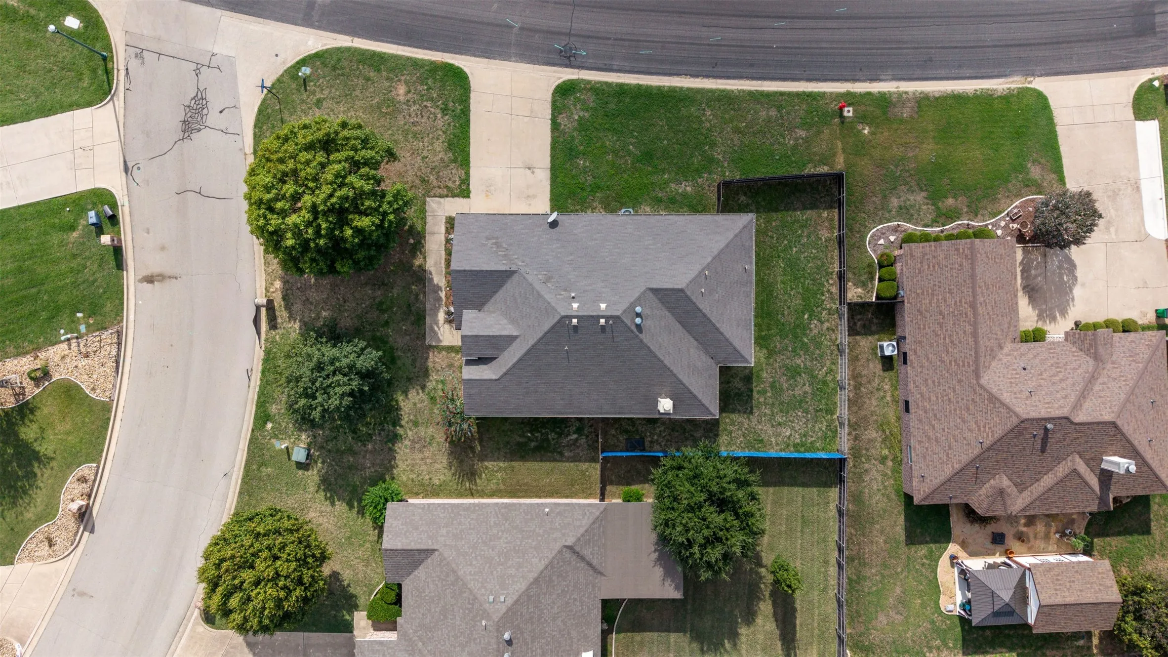 Aerial perspective of a corner lot property featuring a composition shingle roof, paved driveway, concrete walkways, and an enclosed backyard