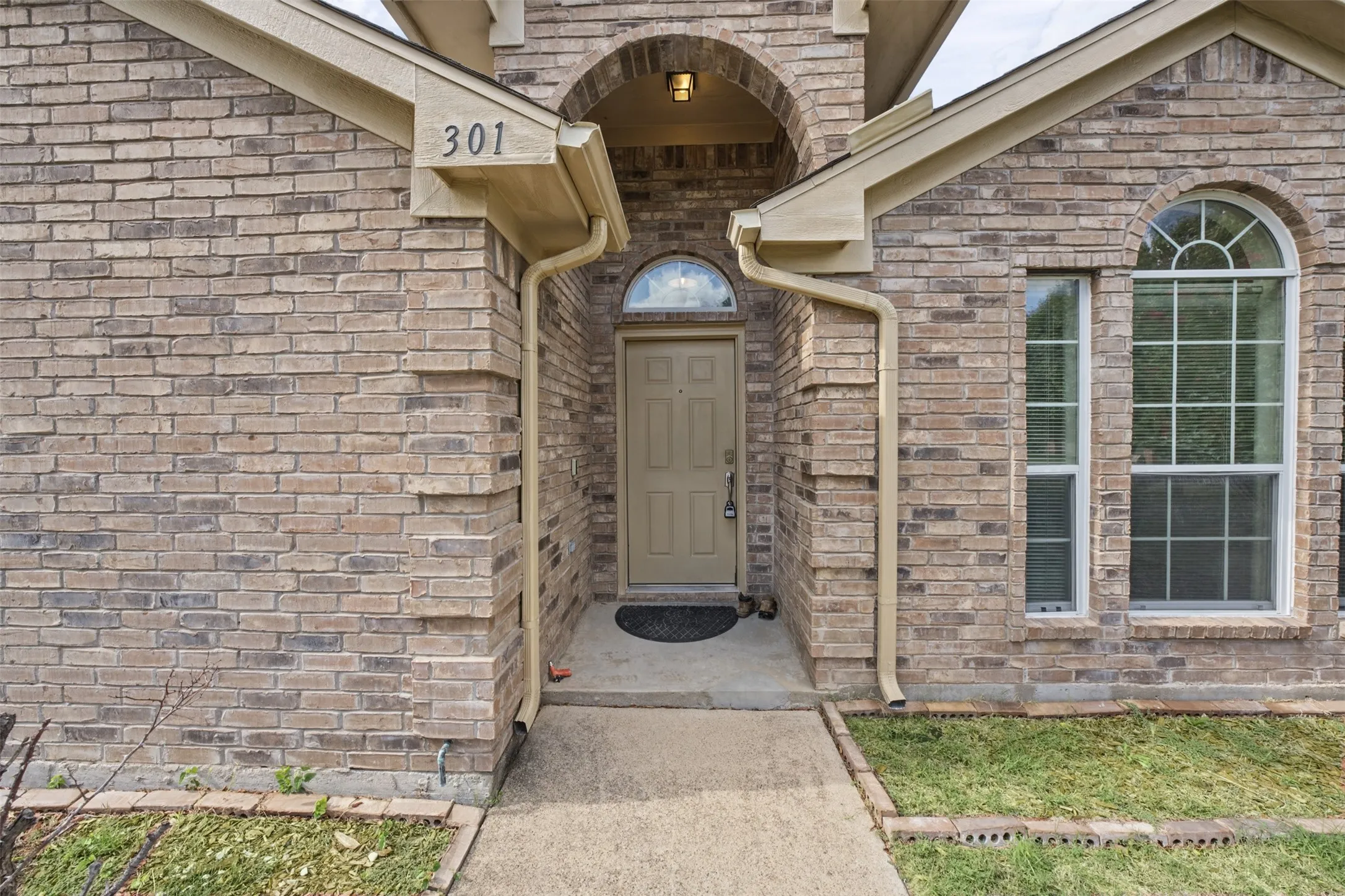 Brick exterior facade featuring a recessed entryway, arched architectural detail above the front door, half-round window, and concrete walkway