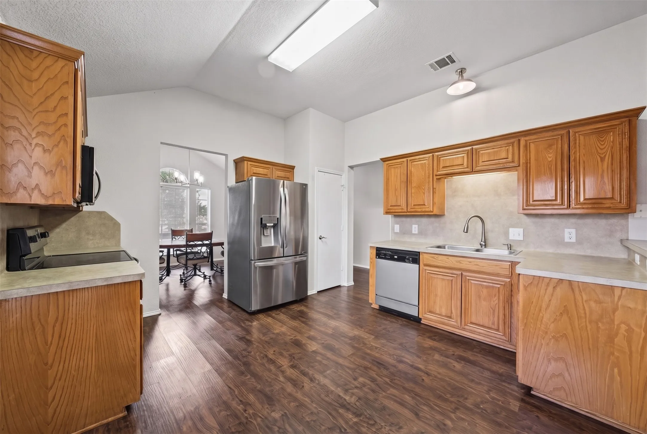 Kitchen featuring wood-finish cabinetry, stainless steel refrigerator and dishwasher, solid-surface countertops, and wood-finish flooring
