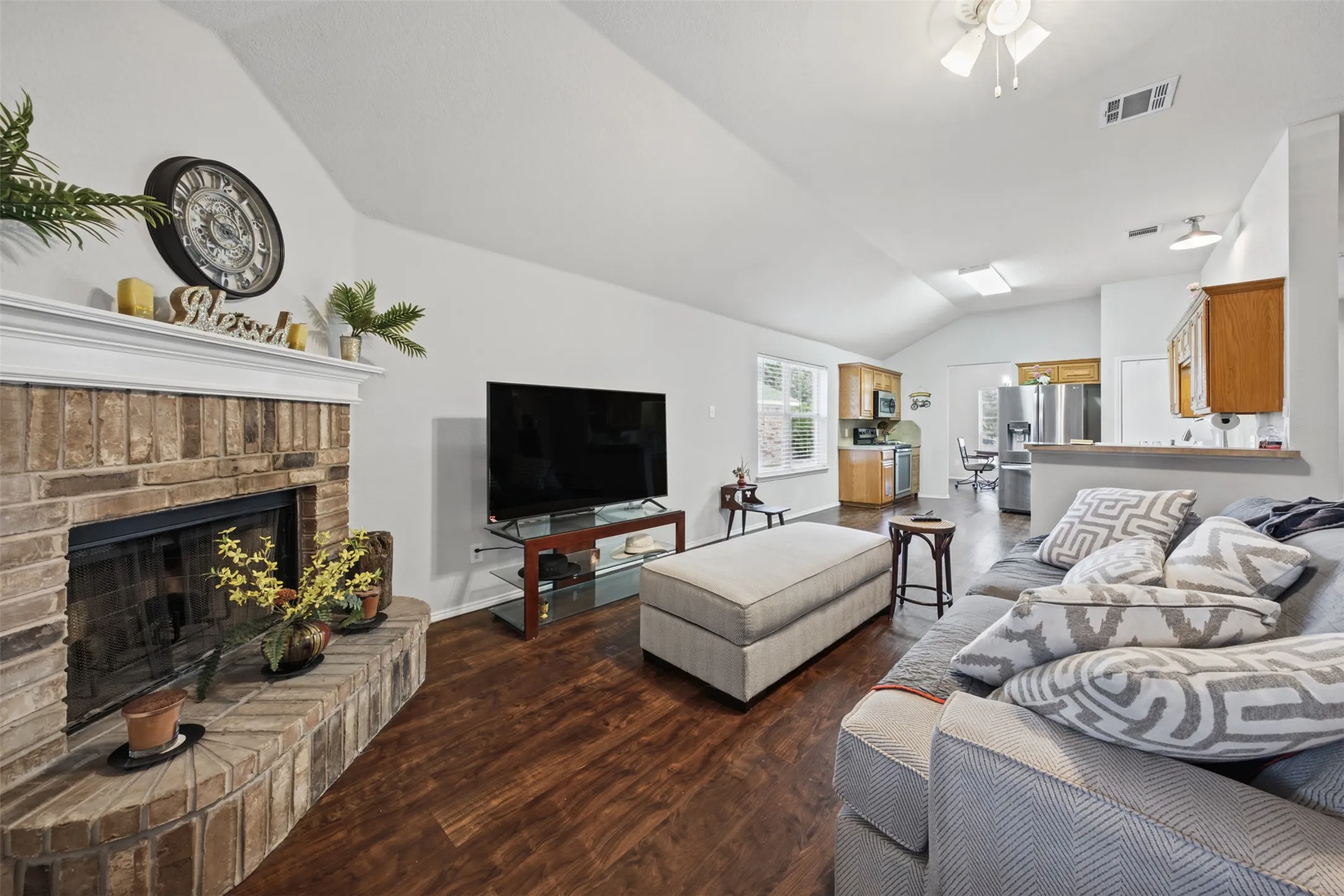 Vaulted ceilings, brick fireplace with a mantle, and dark wood-finish flooring