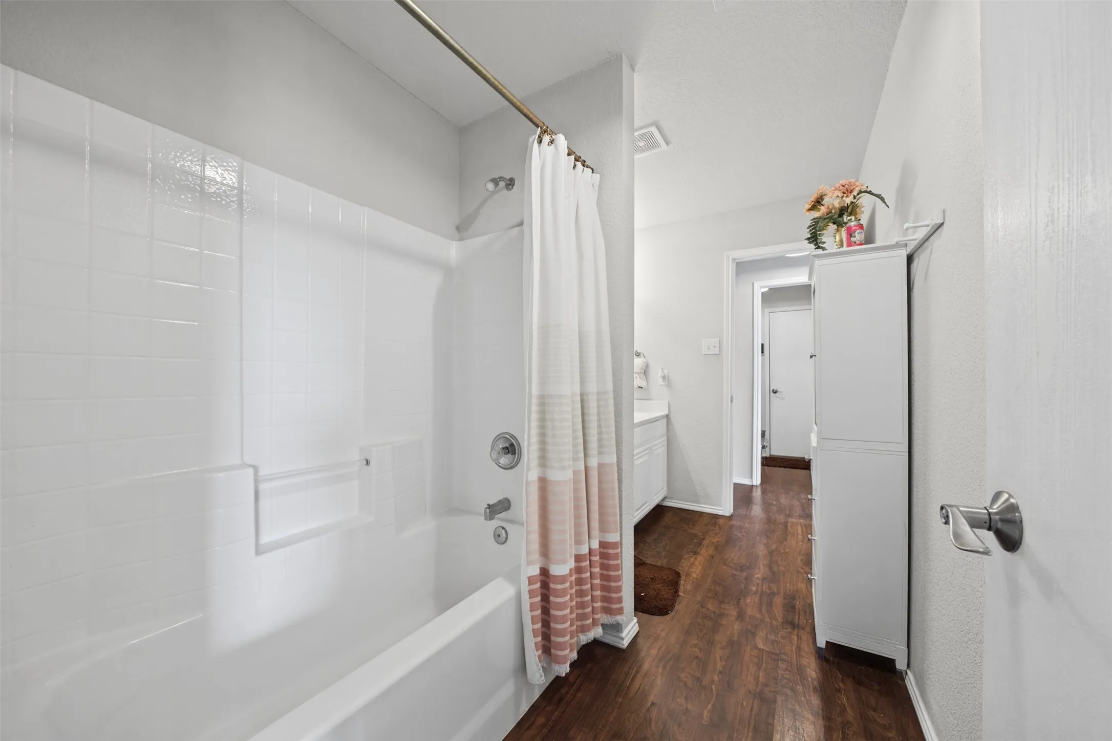 Bathroom featuring a white porcelain tub with tiled surround, wood-finish flooring, and integrated wall cabinetry