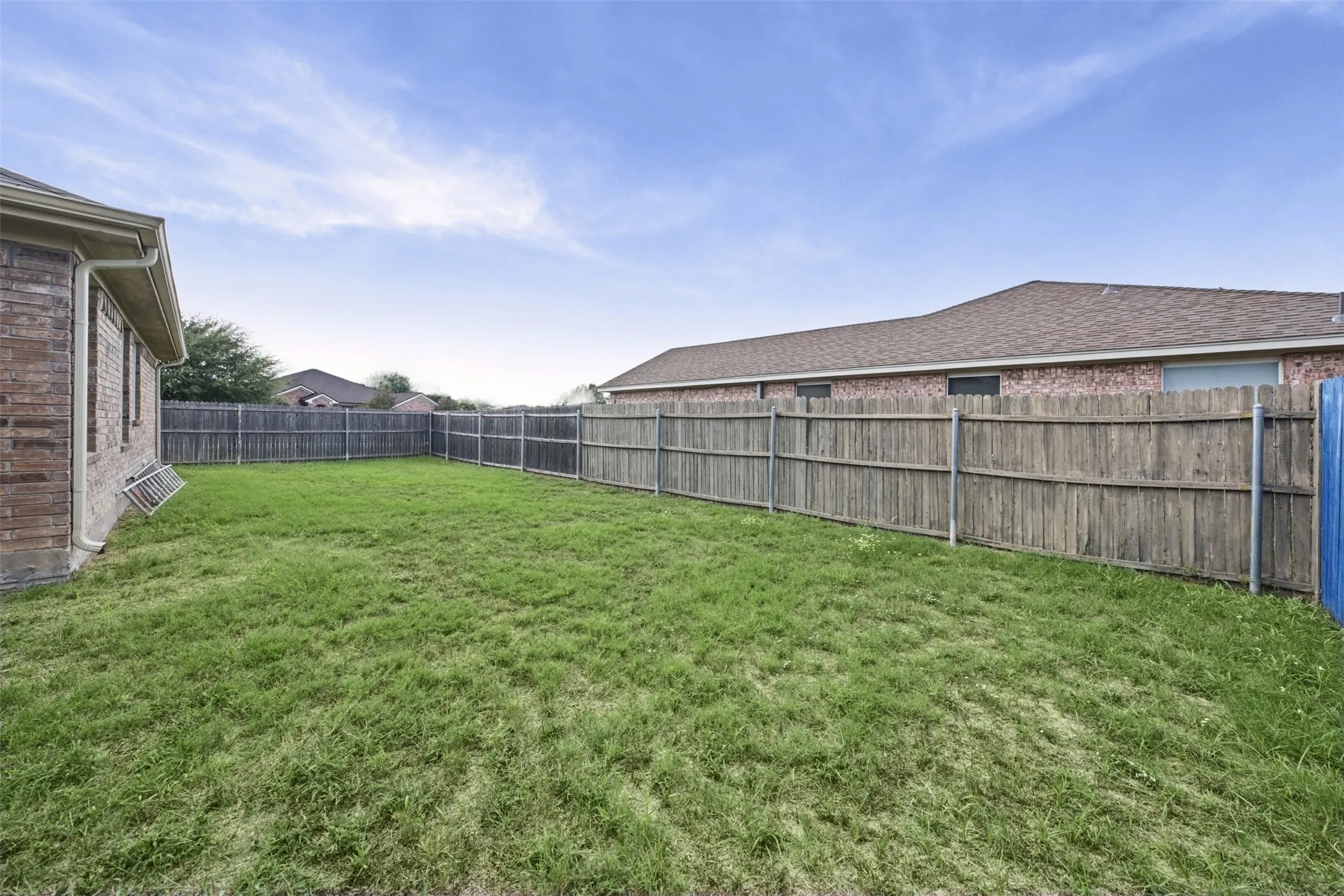 Fenced backyard featuring grass lawn and brick exterior wall