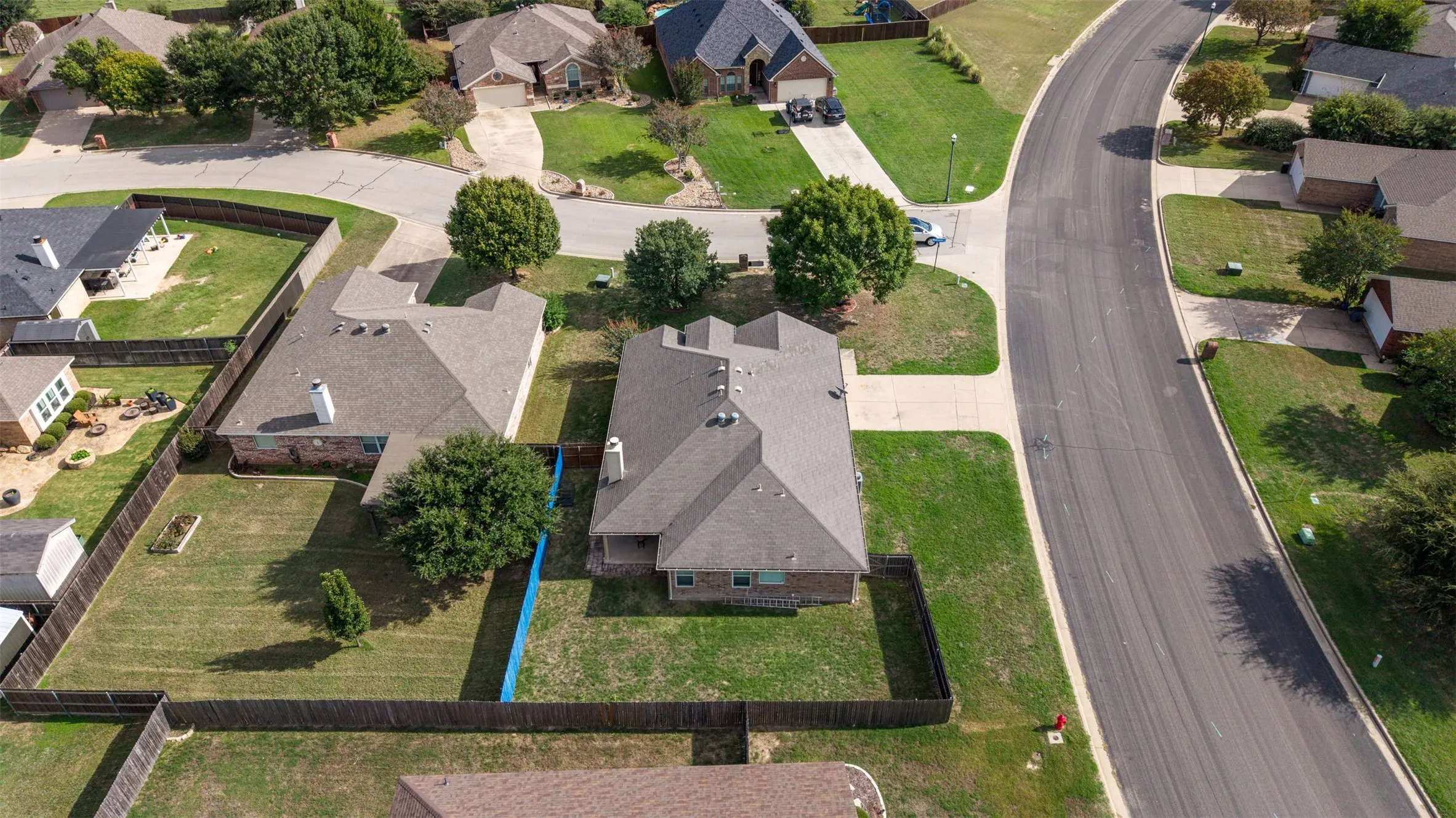 Aerial view of the property featuring a brick exterior, a multi-gabled roof, an attached garage, and a fenced backyard