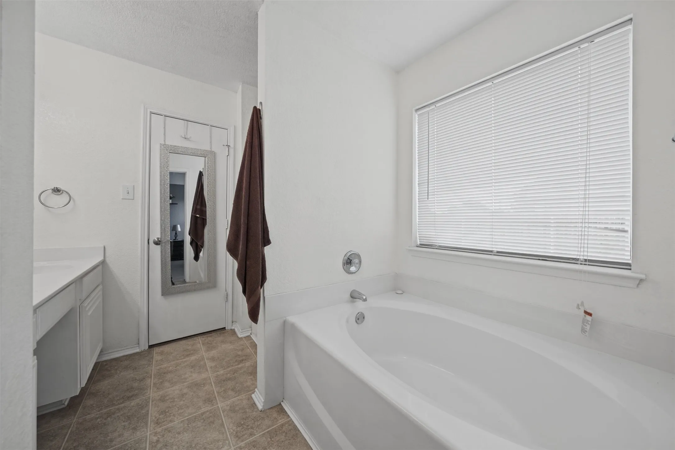 Bathroom featuring an oval soaking tub, ceramic tile flooring, vanity with white cabinetry, and a window with blinds