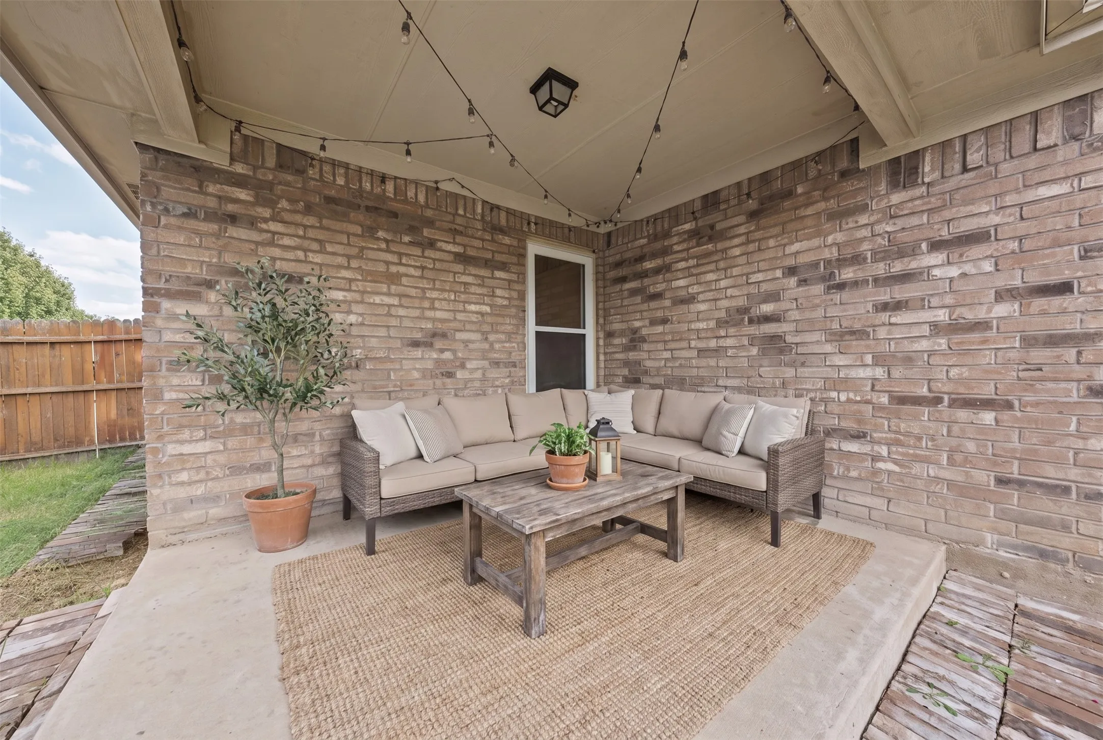 Covered patio featuring a concrete floor, brick masonry walls, and overhead string lighting