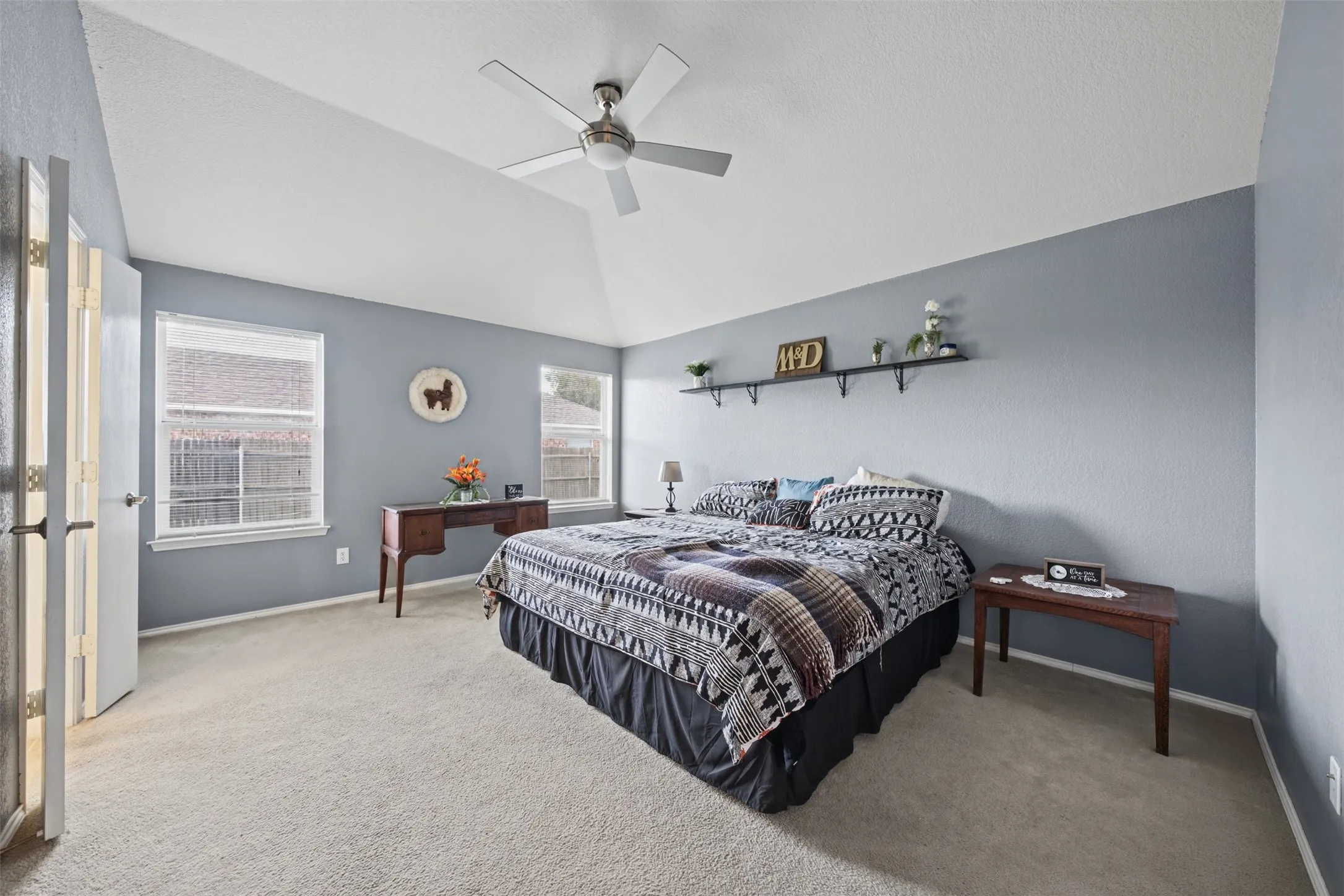 Vaulted ceiling featuring a central brushed-nickel ceiling fan, neutral wall-to-wall carpeting, and dual windows