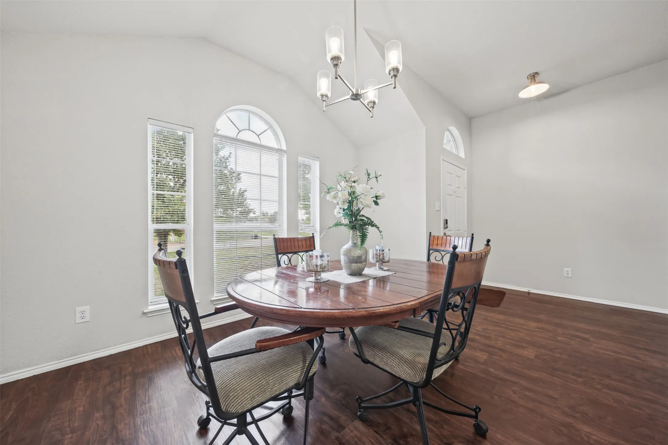 Vaulted ceiling, wood-finish flooring, arch-top windows, and a multi-arm chandelier