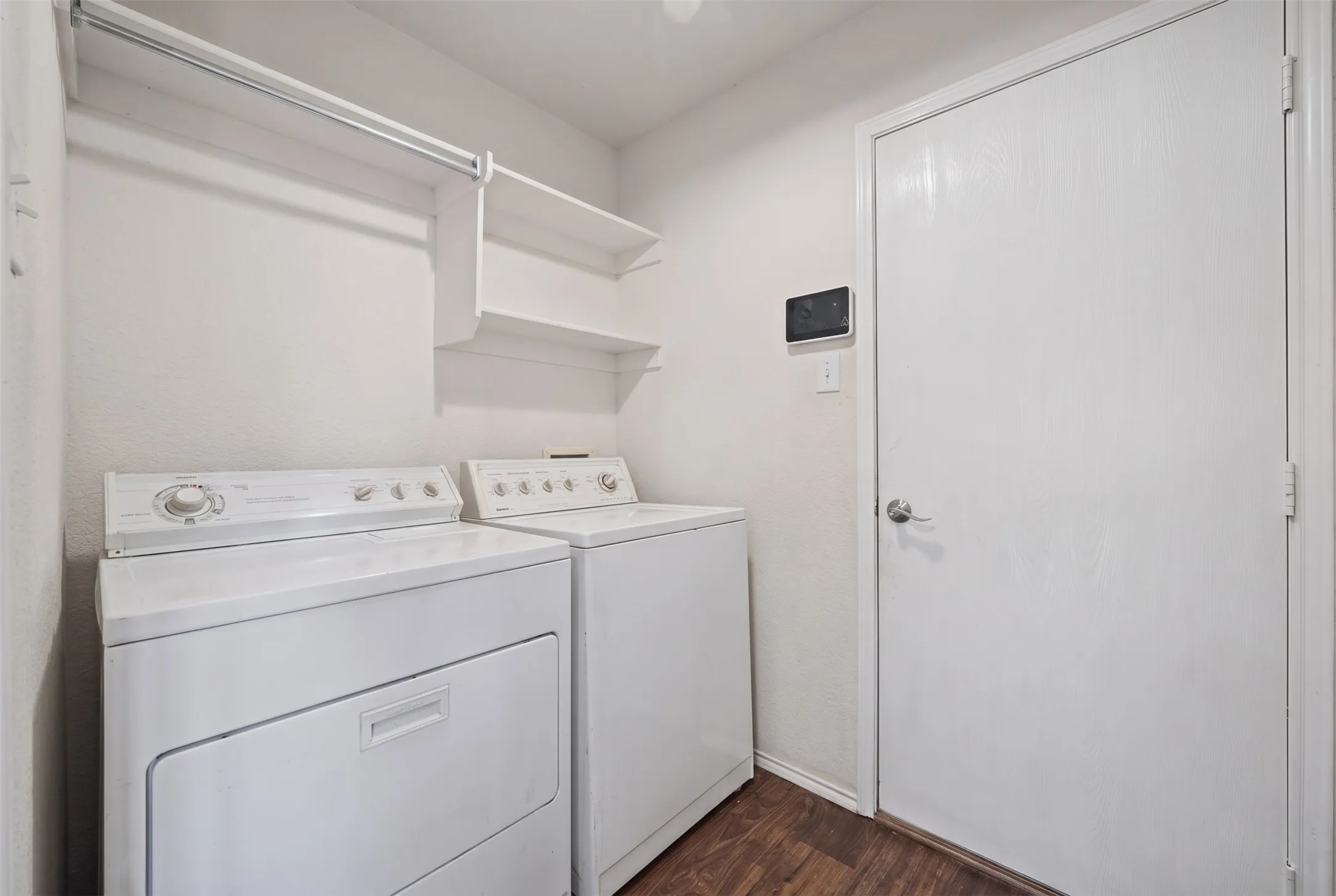 Dedicated laundry area featuring wood-finish flooring, built-in shelving, and a wall-mounted control panel