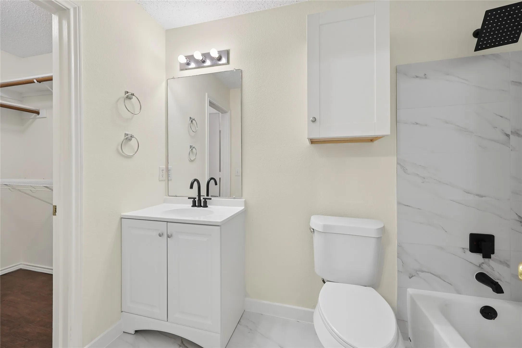 Bathroom featuring a white vanity with a rectangular sink, matte black fixtures, a wall-mounted storage cabinet, and tub surround with stone-finish tile